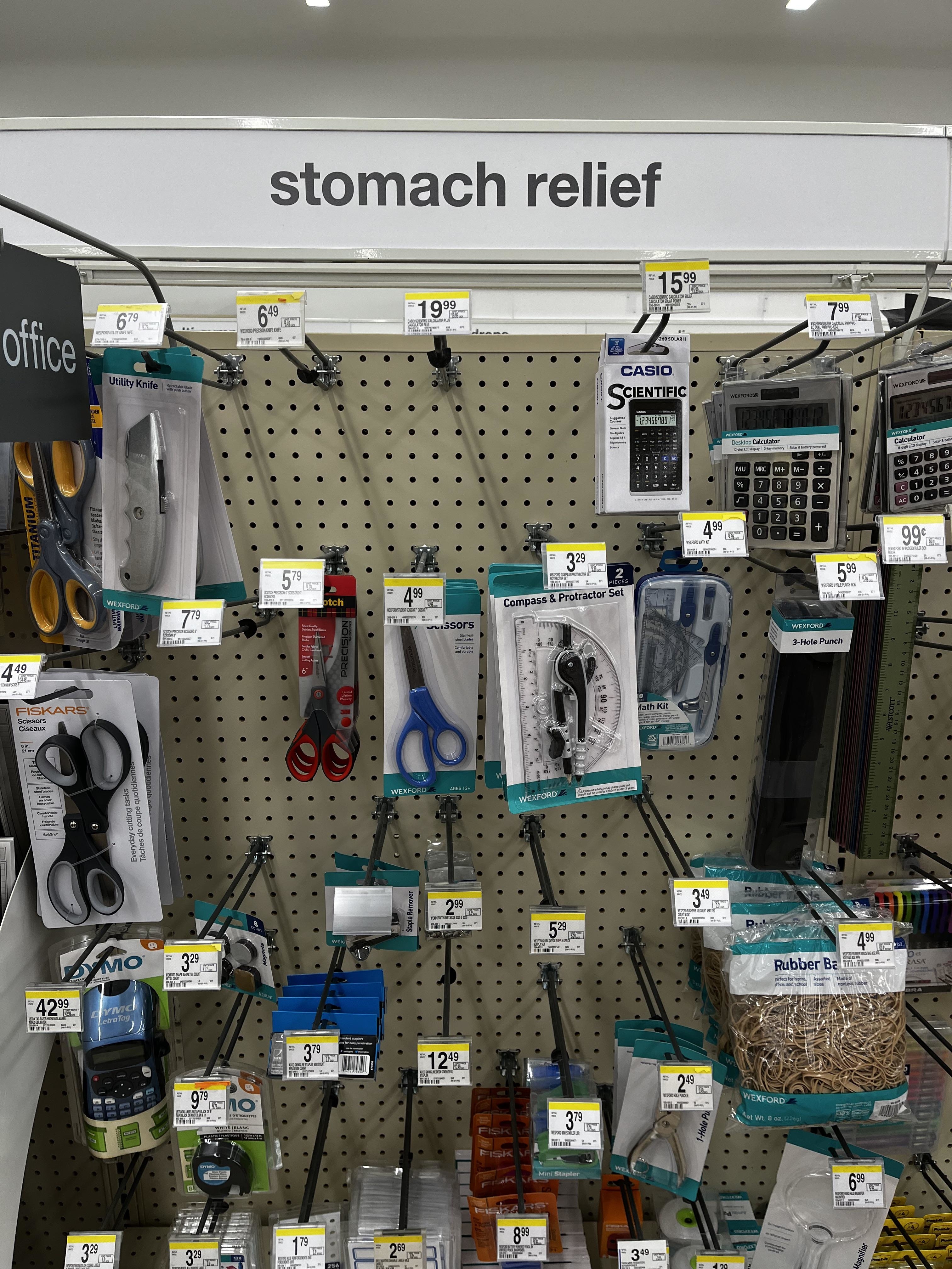 A store shelf labeled &quot;stomach relief&quot; mistakenly stocked with office supplies, including scissors, calculators, and staplers