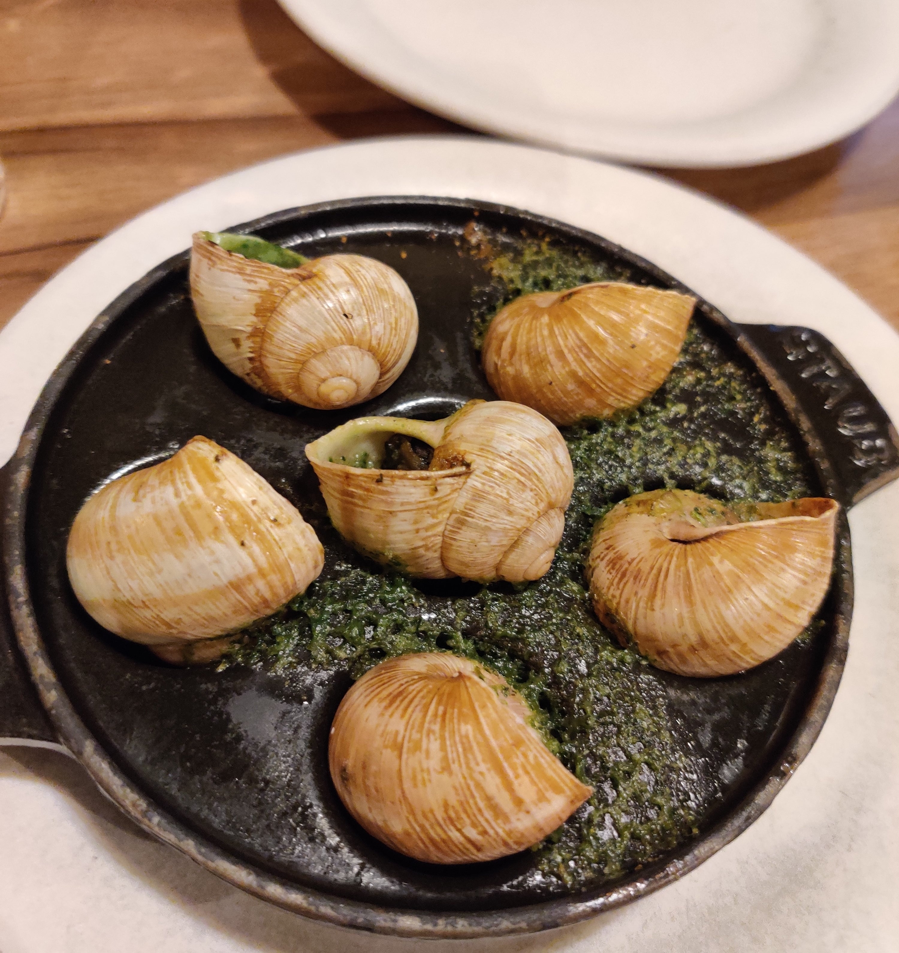A plate of escargot cooked with garlic and herb butter, served in a round dish on a white plate