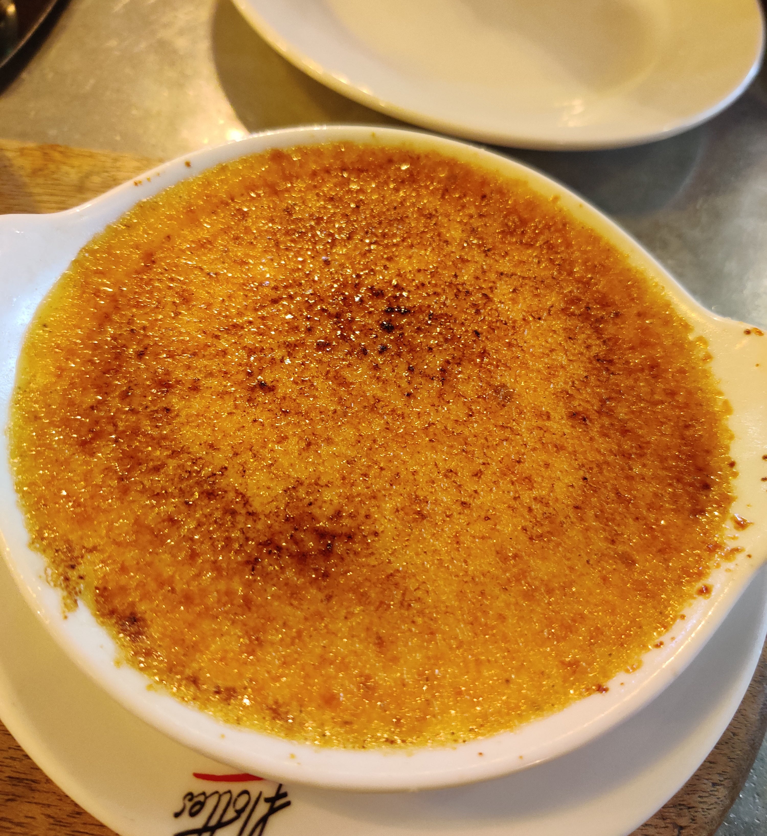 A dish of crème brûlée with a caramelized sugar topping served on a white plate