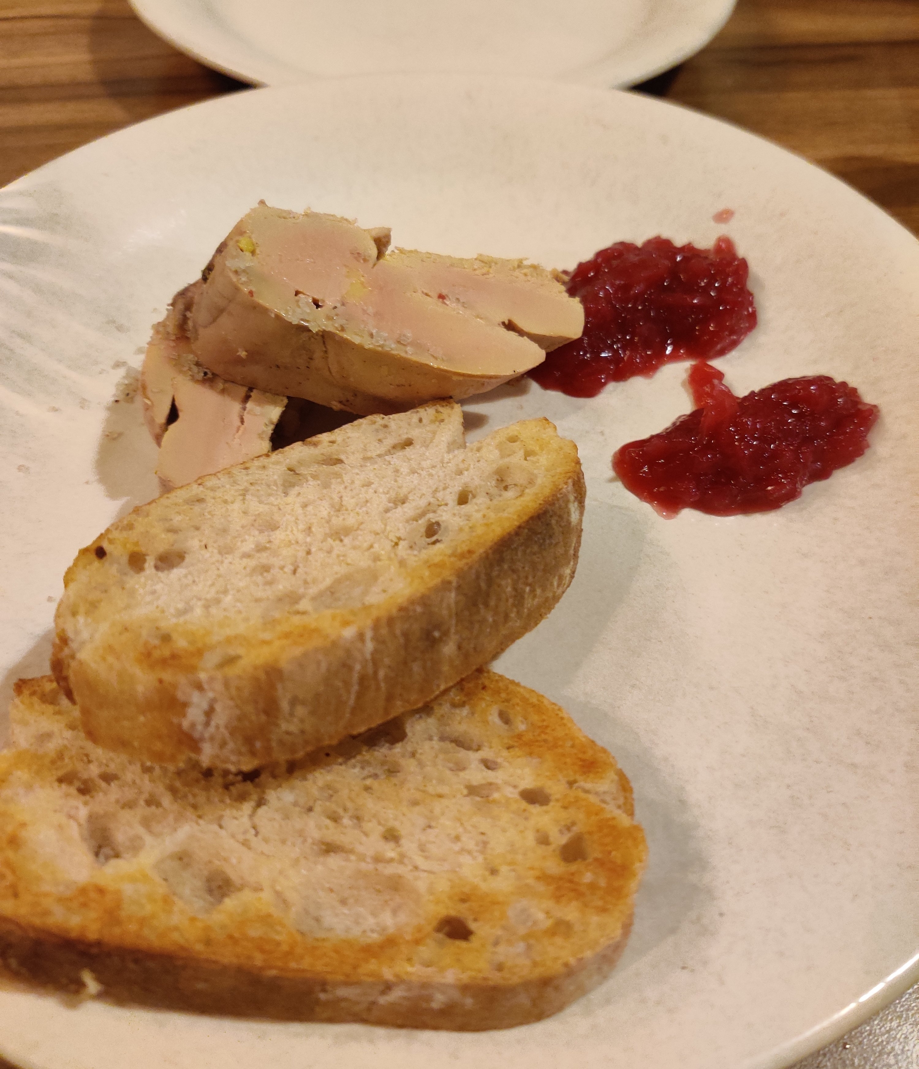 Slices of bread and foie gras with two dollops of red jam on a white plate