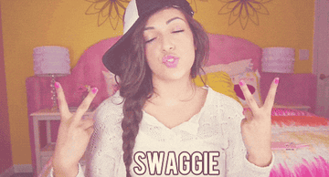 A young woman in a casual outfit and sideways cap makes peace signs with both hands while puckering her lips. The word &quot;SWAGGIE&quot; is shown