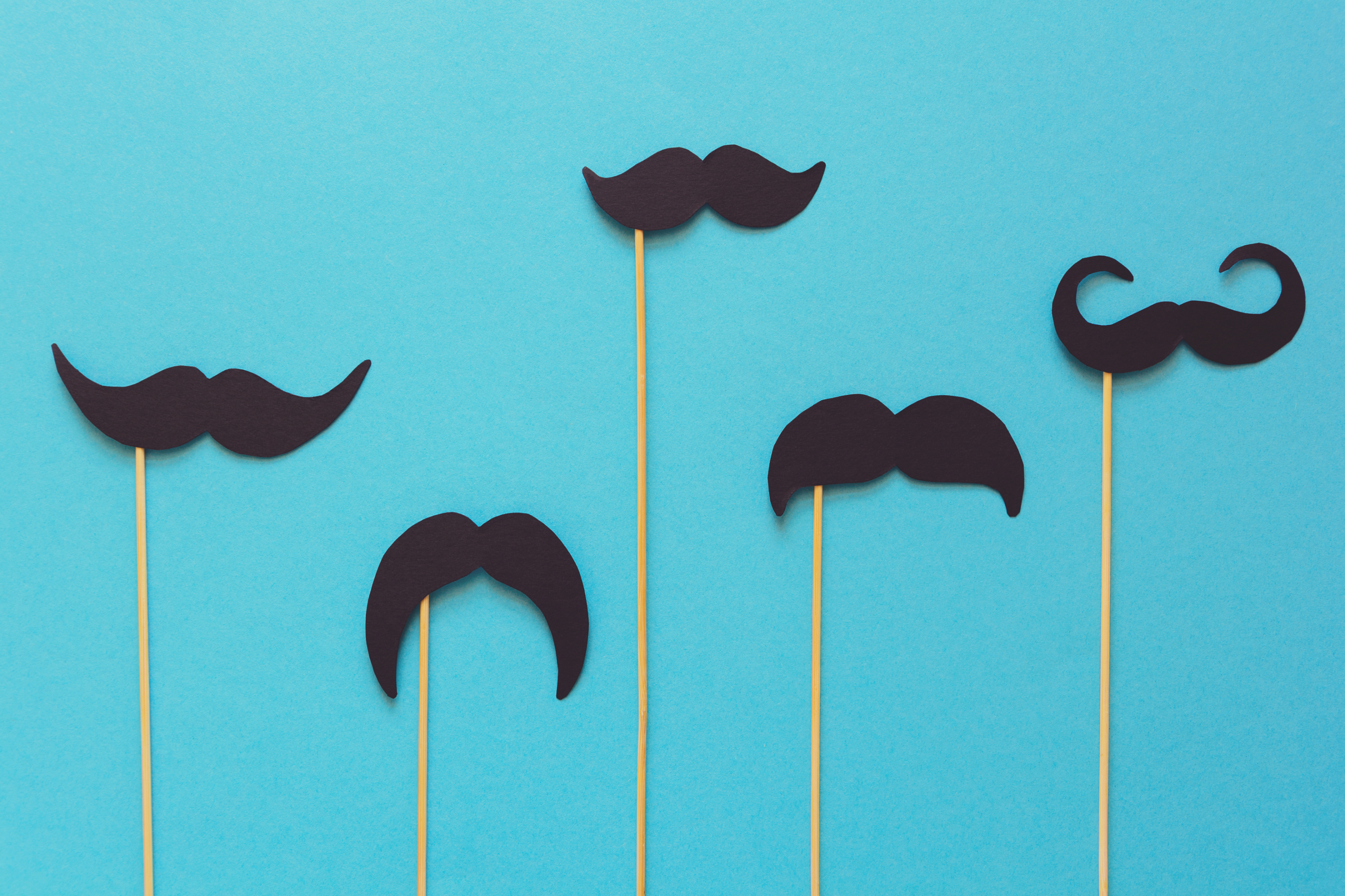 Image of five black paper mustaches on sticks, arranged against a plain background
