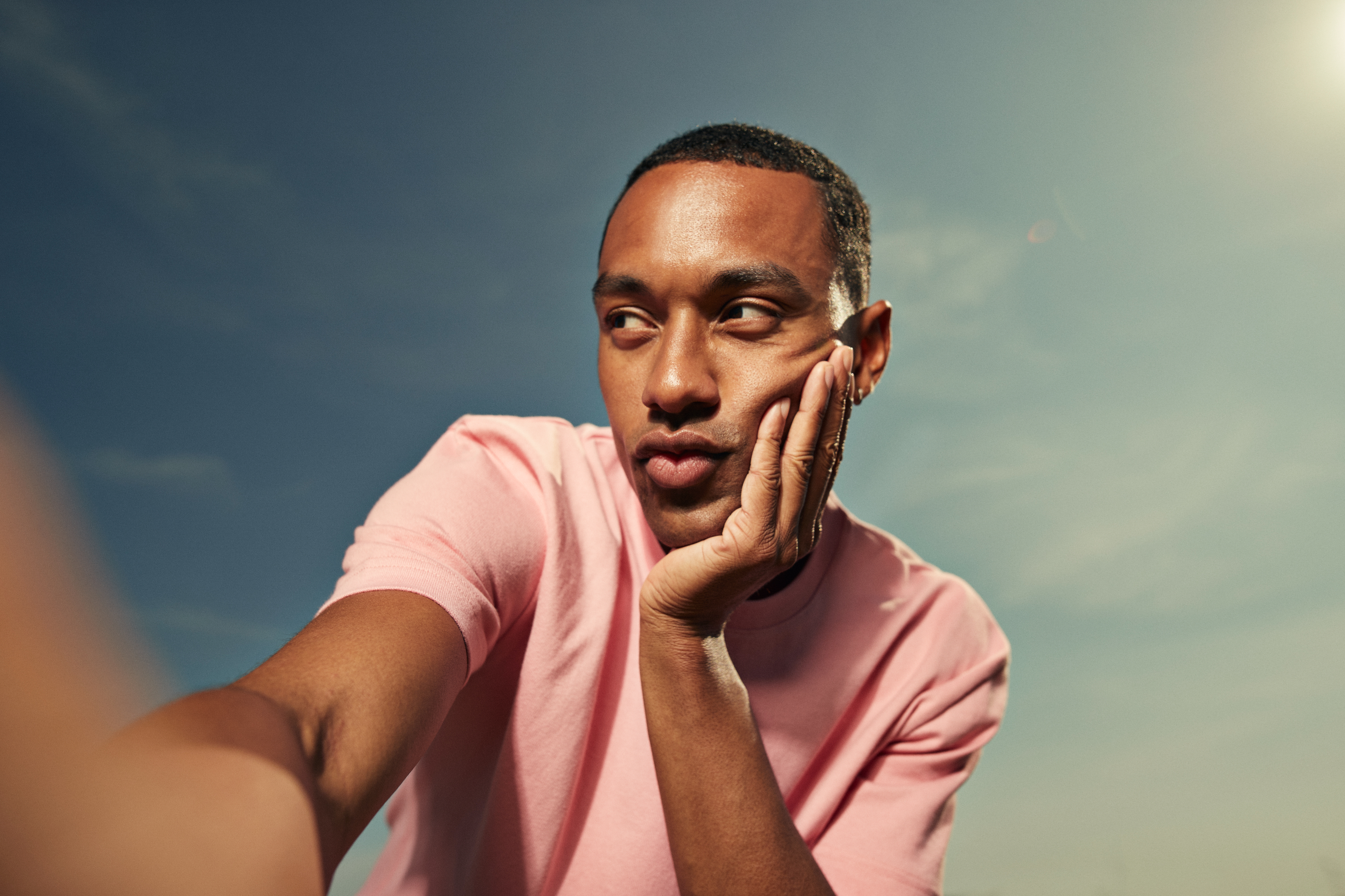 A person in a pink shirt gazes pensively into the distance, resting their chin on their hand