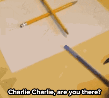 A pencil cross game setup on a table with two pencils forming a cross over a paper. Text reads, &quot;Charlie Charlie, are you there?&quot;