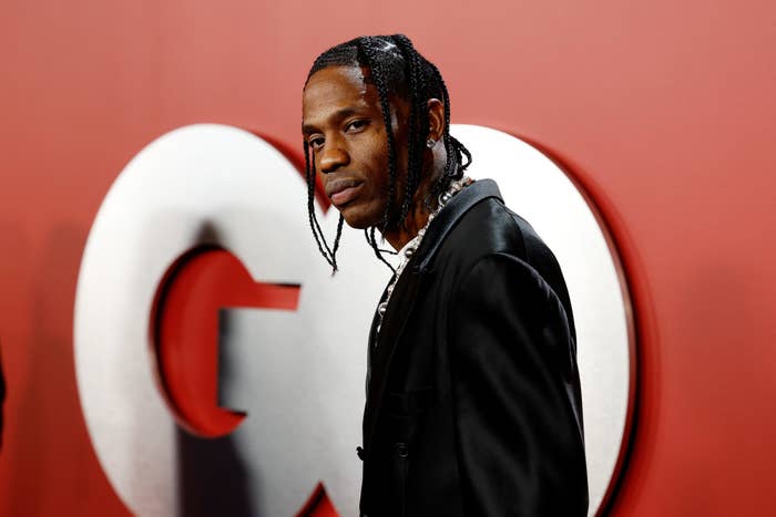 Travis Scott on the red carpet at a GQ event, wearing a sleek dark suit with braided hair