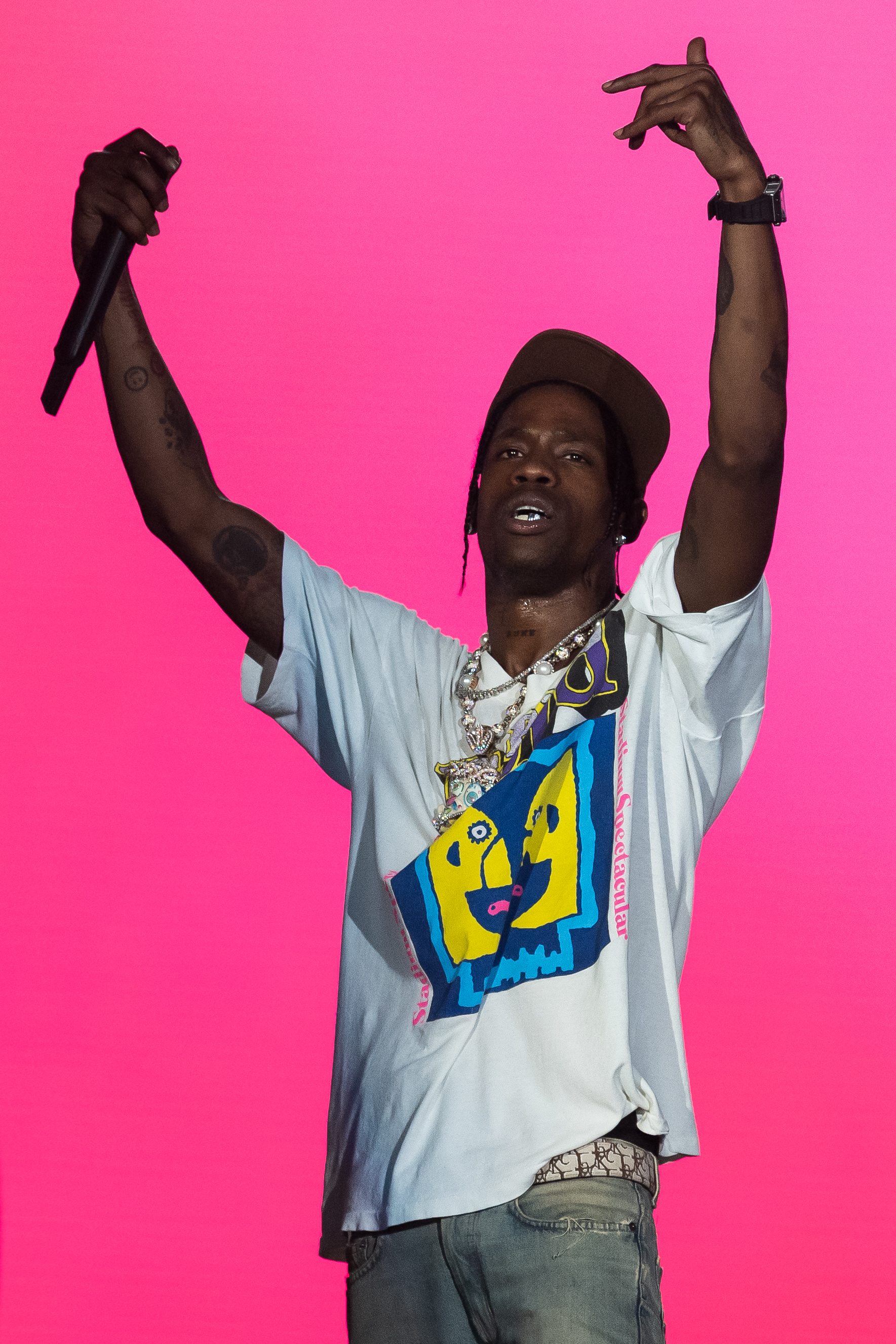 Travis Scott performing on stage, dressed casually in a graphic t-shirt, jeans, and cap, with a microphone in hand