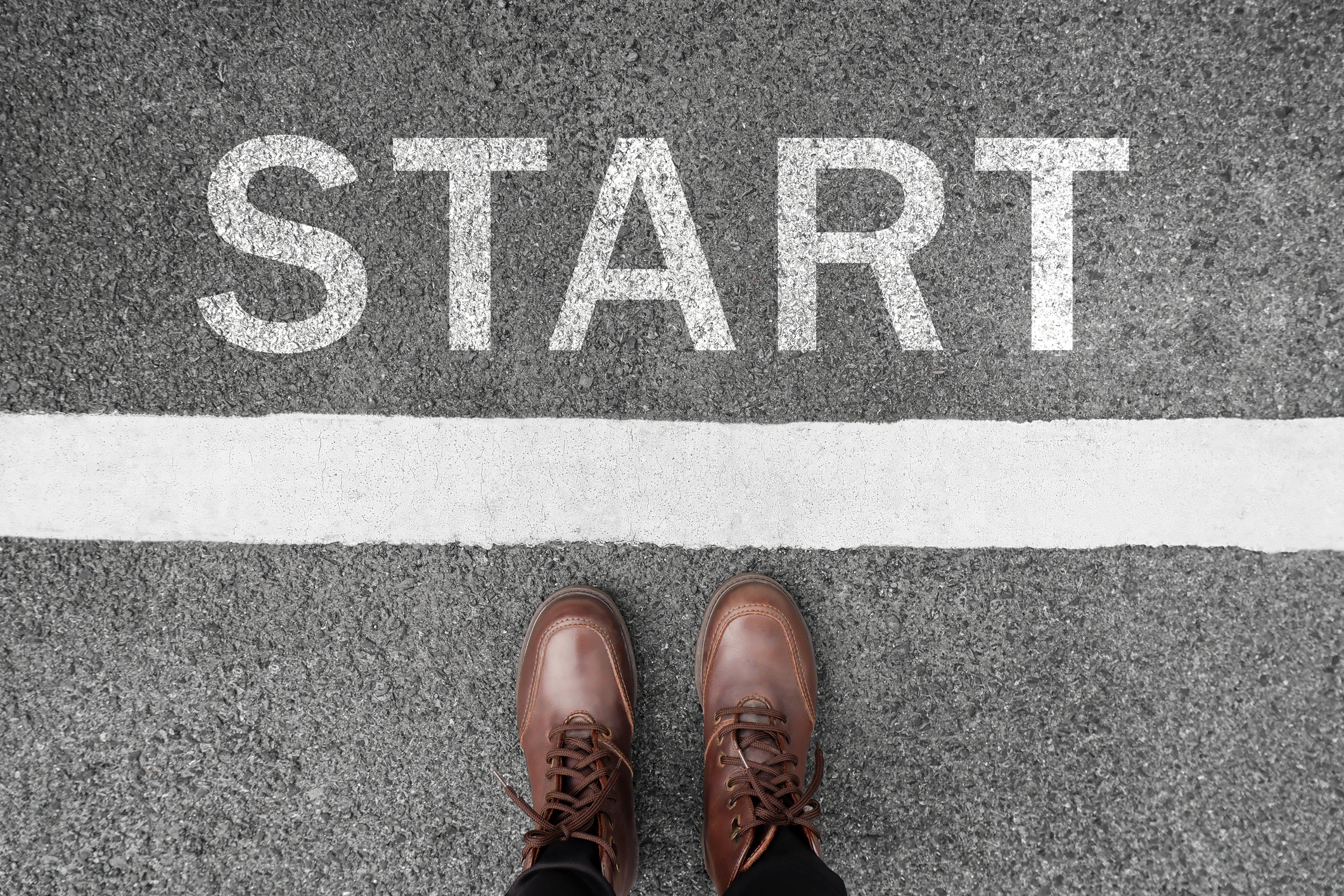 Person wearing brown shoes standing at a starting line on a paved surface with the word &quot;START&quot; written in large white letters on the ground