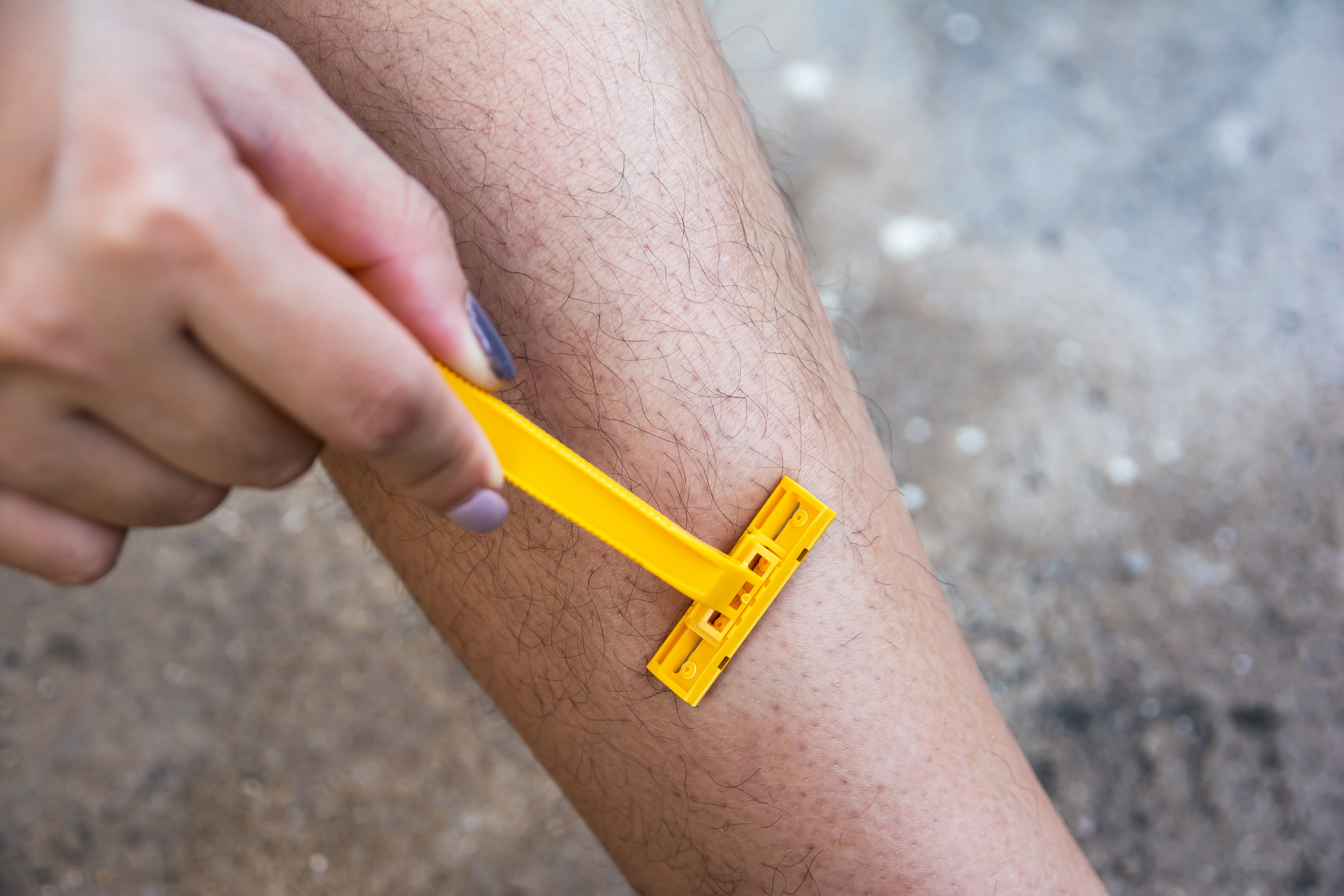 A close-up of a person using a yellow razor to shave their leg