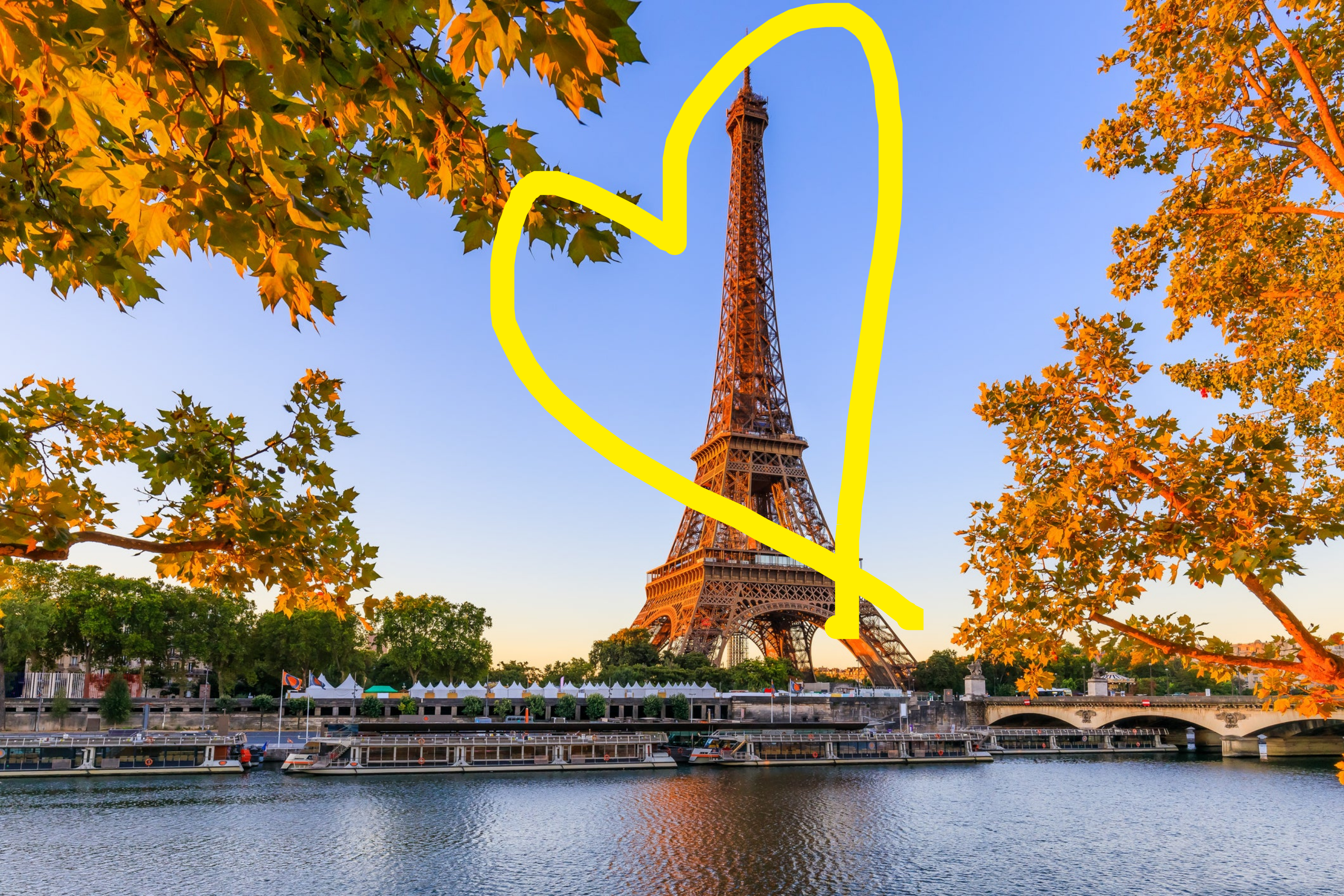 The Eiffel Tower standing tall by the Seine River with boats docked at the riverside, surrounded by trees