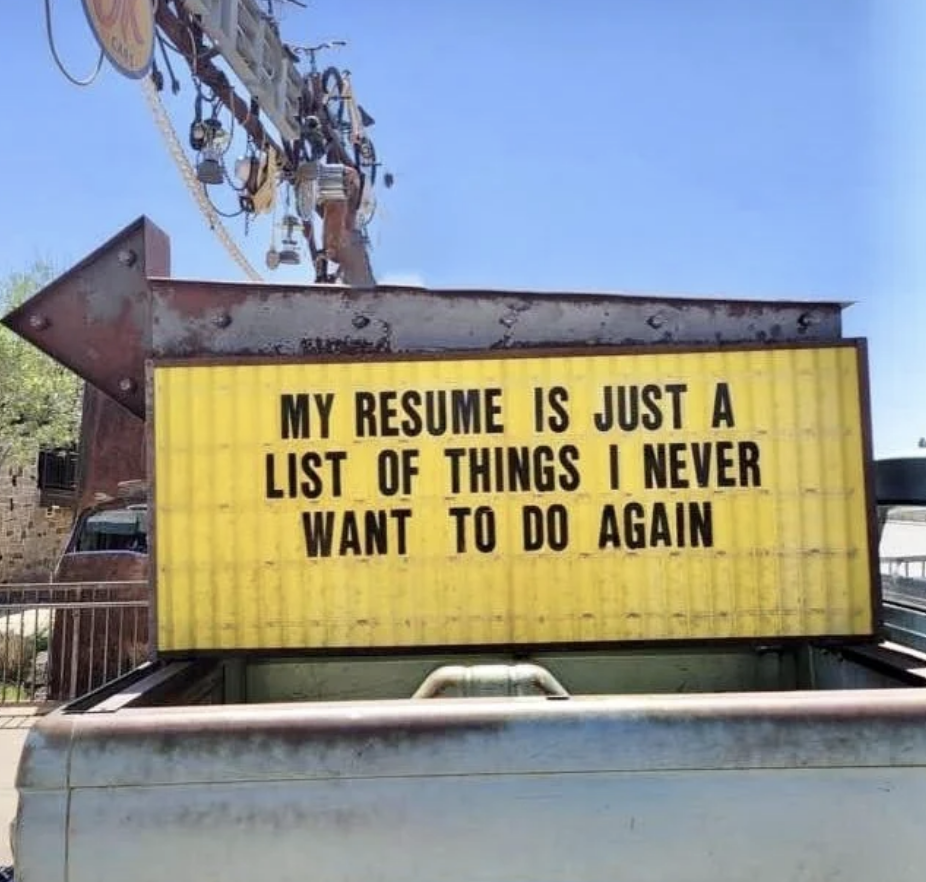 A large sign reads, &quot;My resume is just a list of things I never want to do again.&quot; The sign is mounted on a structure near some industrial equipment