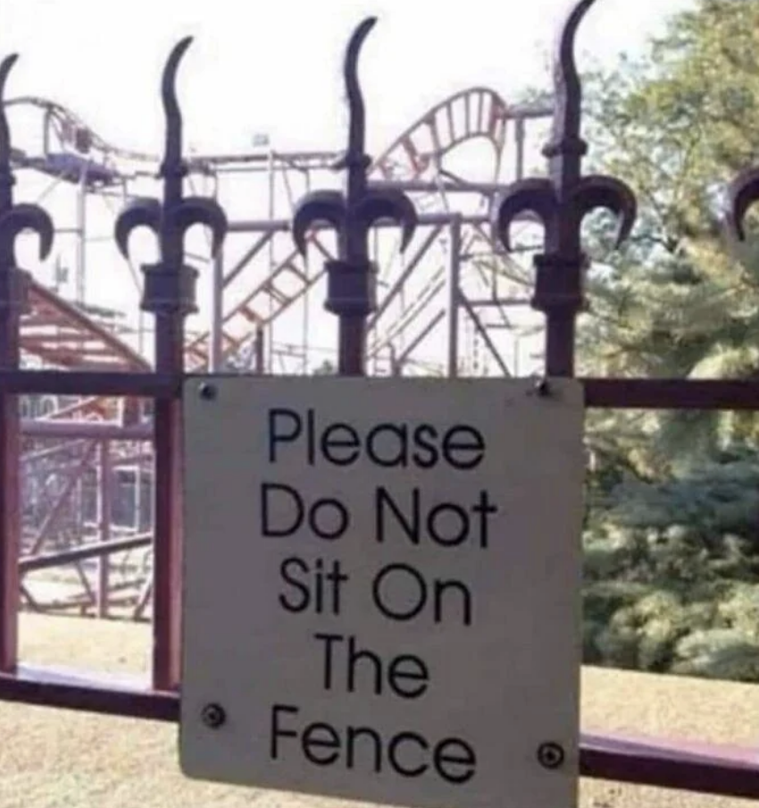 Sign on a fence that reads, &quot;Please Do Not Sit On The Fence,&quot; with a roller coaster visible in the background
