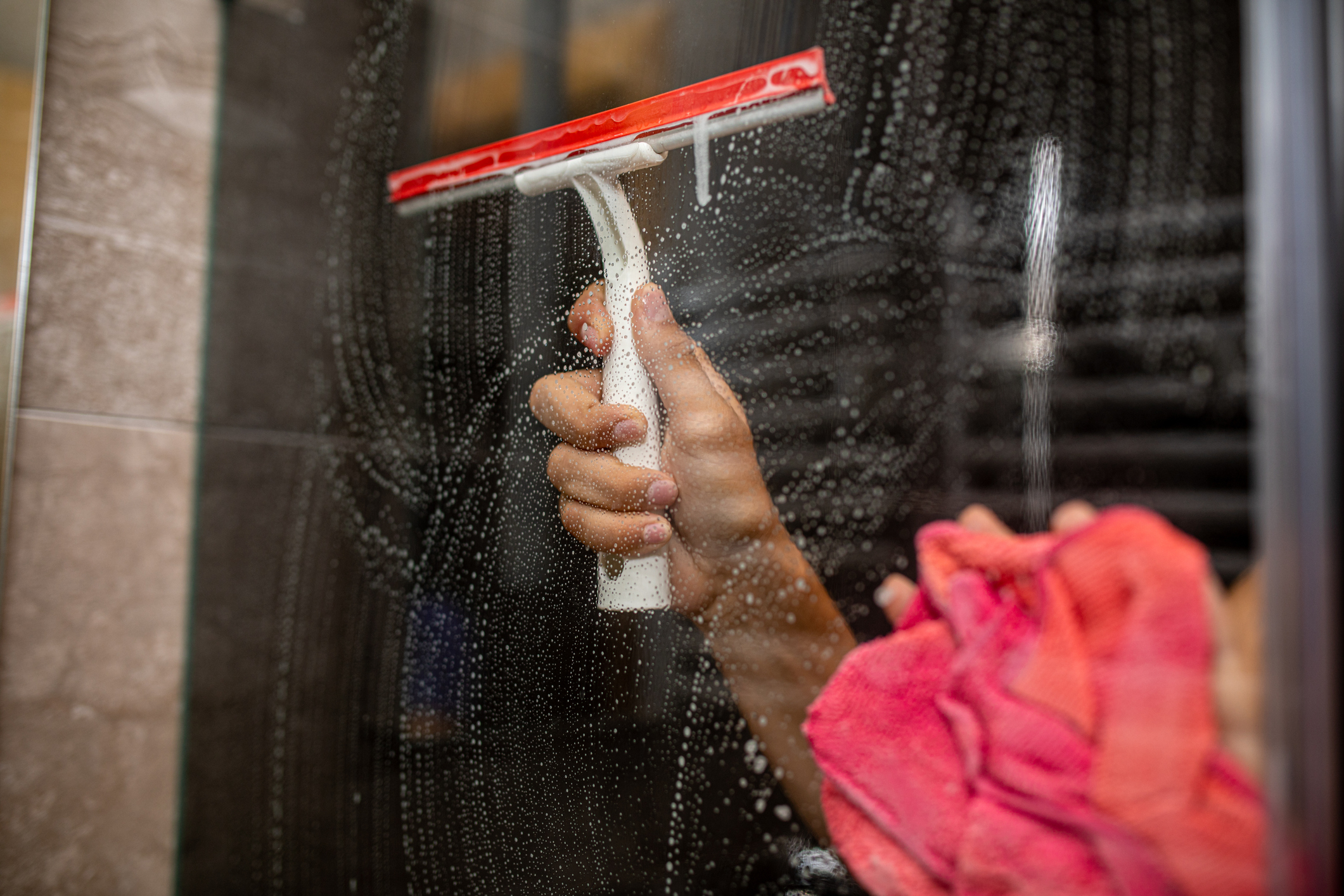 A person cleaning a glass surface with a squeegee and holding a pink cloth