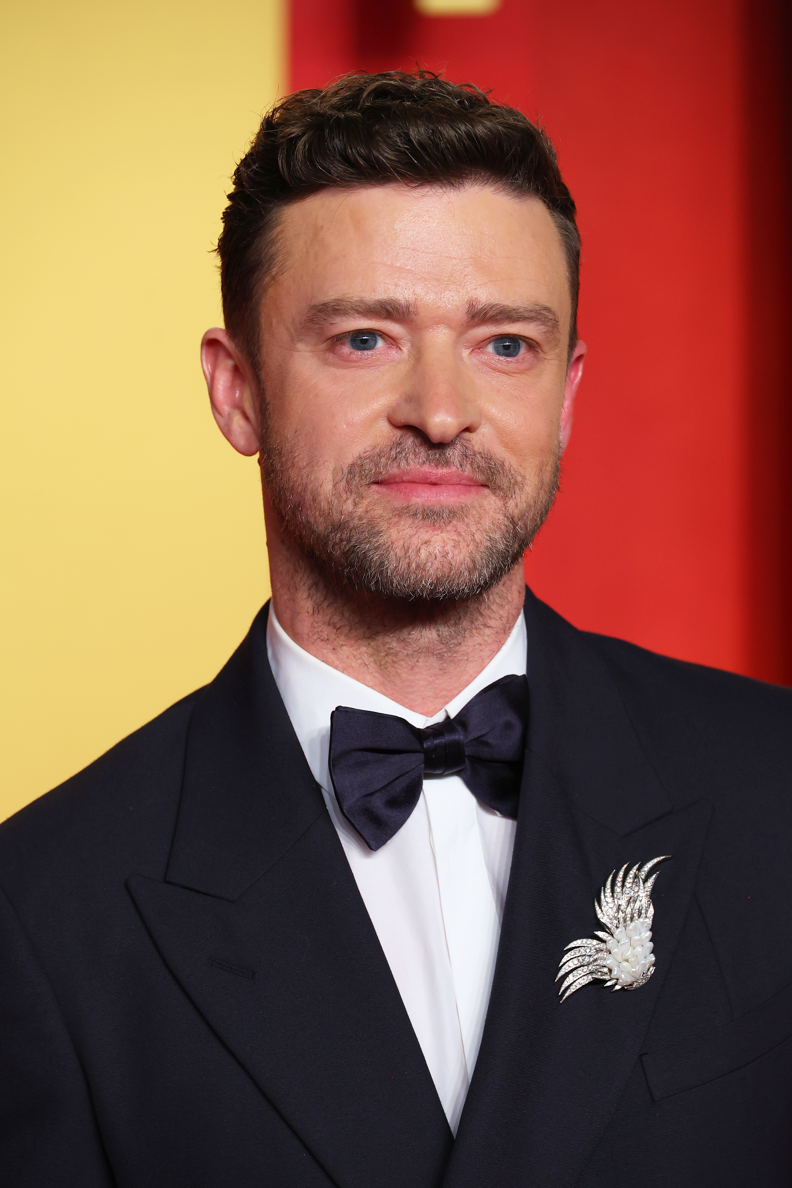 Justin Timberlake dressed in a black tuxedo with a bow tie and decorative brooch at a red carpet event