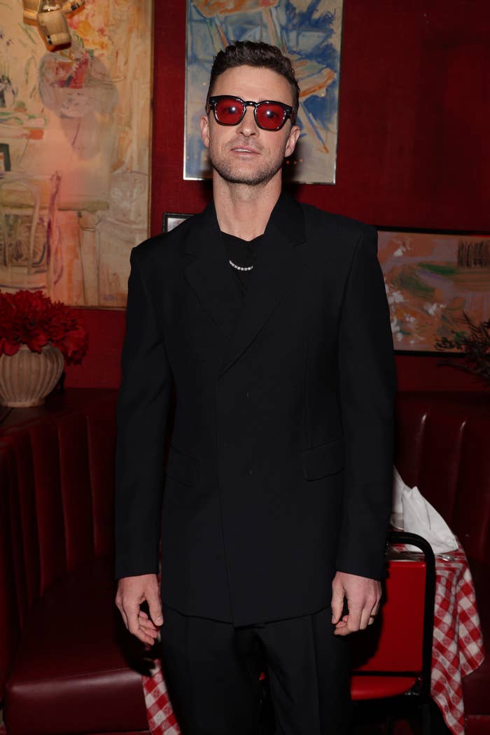 Justin Timberlake wearing sunglasses and a black suit poses indoors at a red carpet event