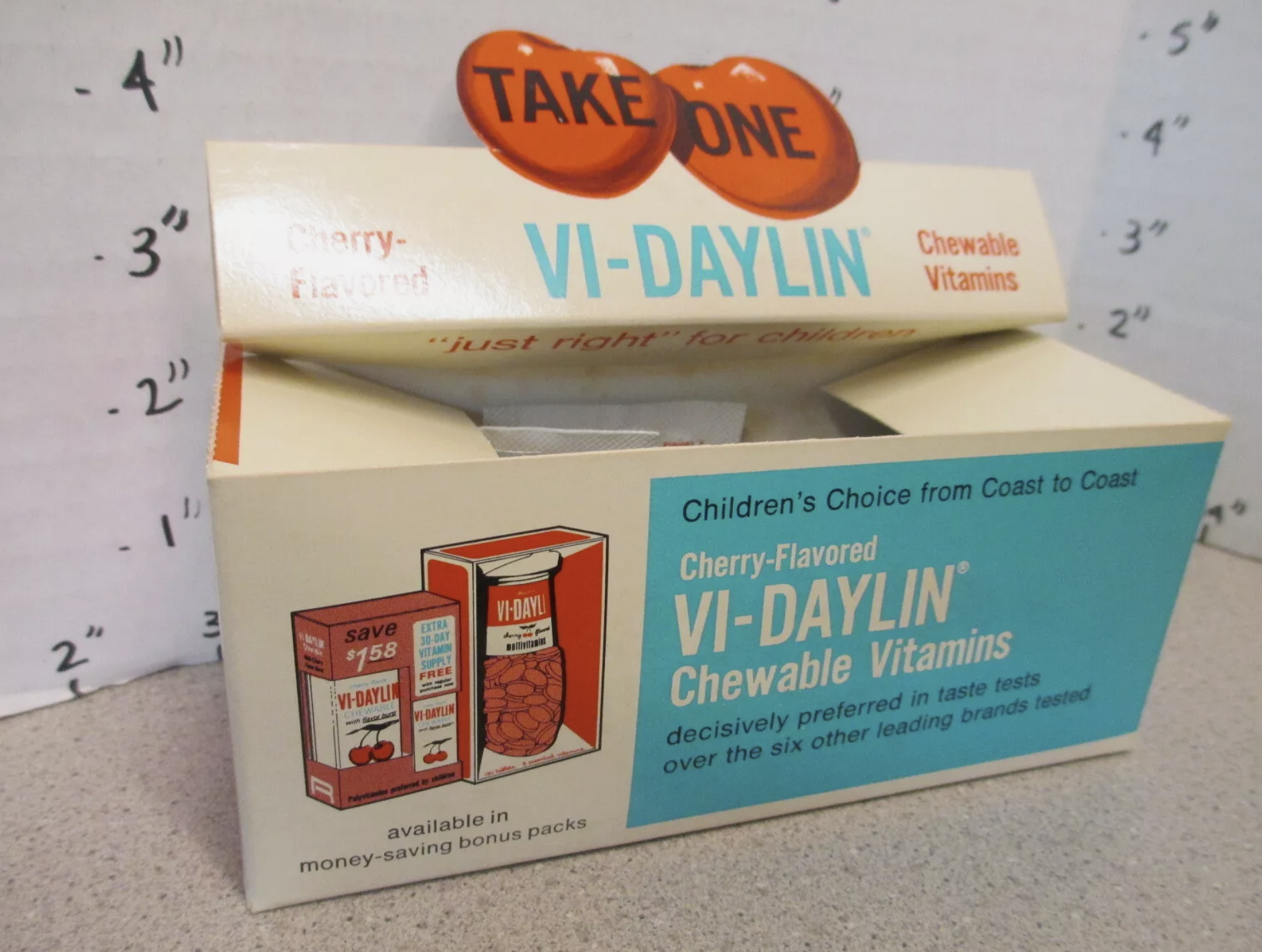 Box of Vi-Daylin cherry-flavored chewable vitamins for children, with &quot;Take One&quot; sign on top. The box highlights availability in money-saving bonus packs