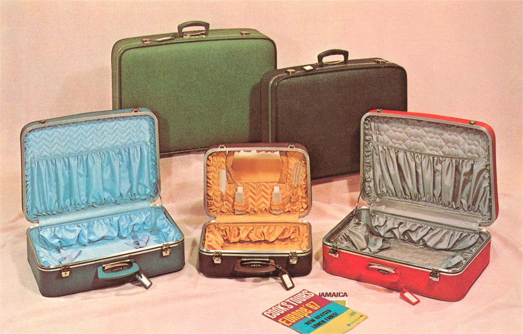 Three open and two closed vintage suitcases. The open suitcases reveal patterned linings. A paper labeled &quot;Travel Tips Jamaica&quot; is in front