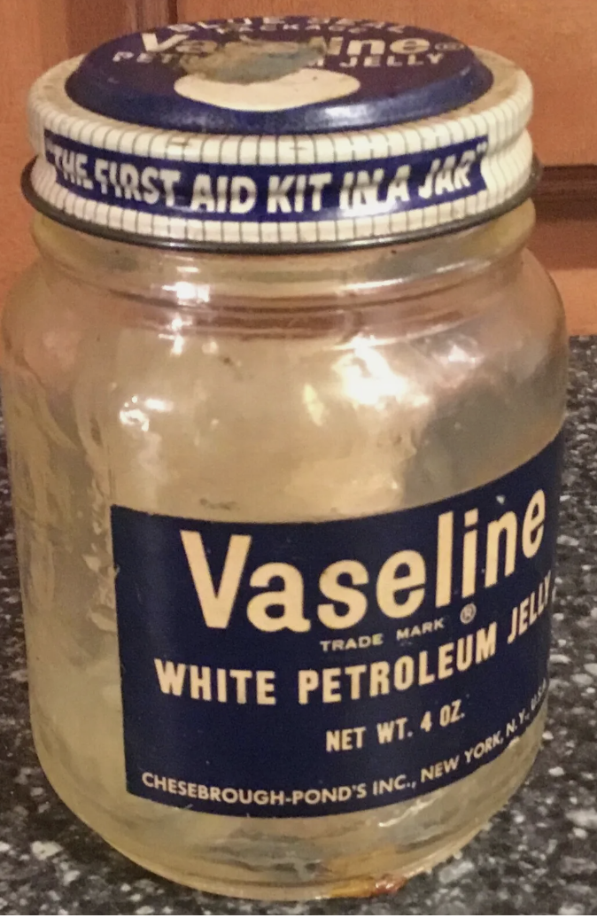 A vintage jar of Vaseline White Petroleum Jelly with the label &quot;The First Aid Kit in a Jar&quot; on the lid. The jar is 4 oz by Chesebrough-Pond&#x27;s Inc