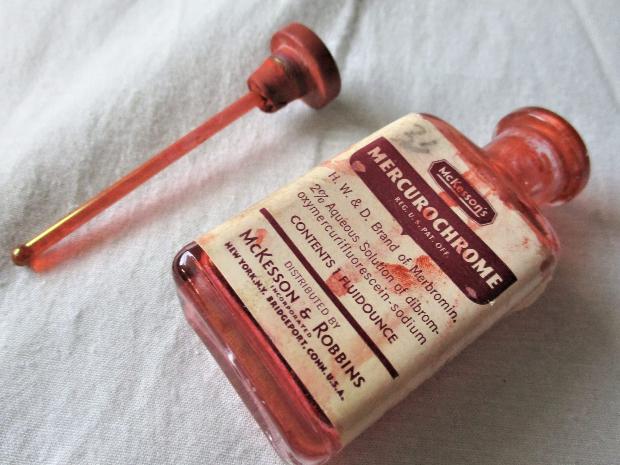 A vintage bottle of Mercurochrome antiseptic with a glass dropper detached. The label shows 2% aqueous solution and manufacturer details: McKesson &amp;amp; Robbins