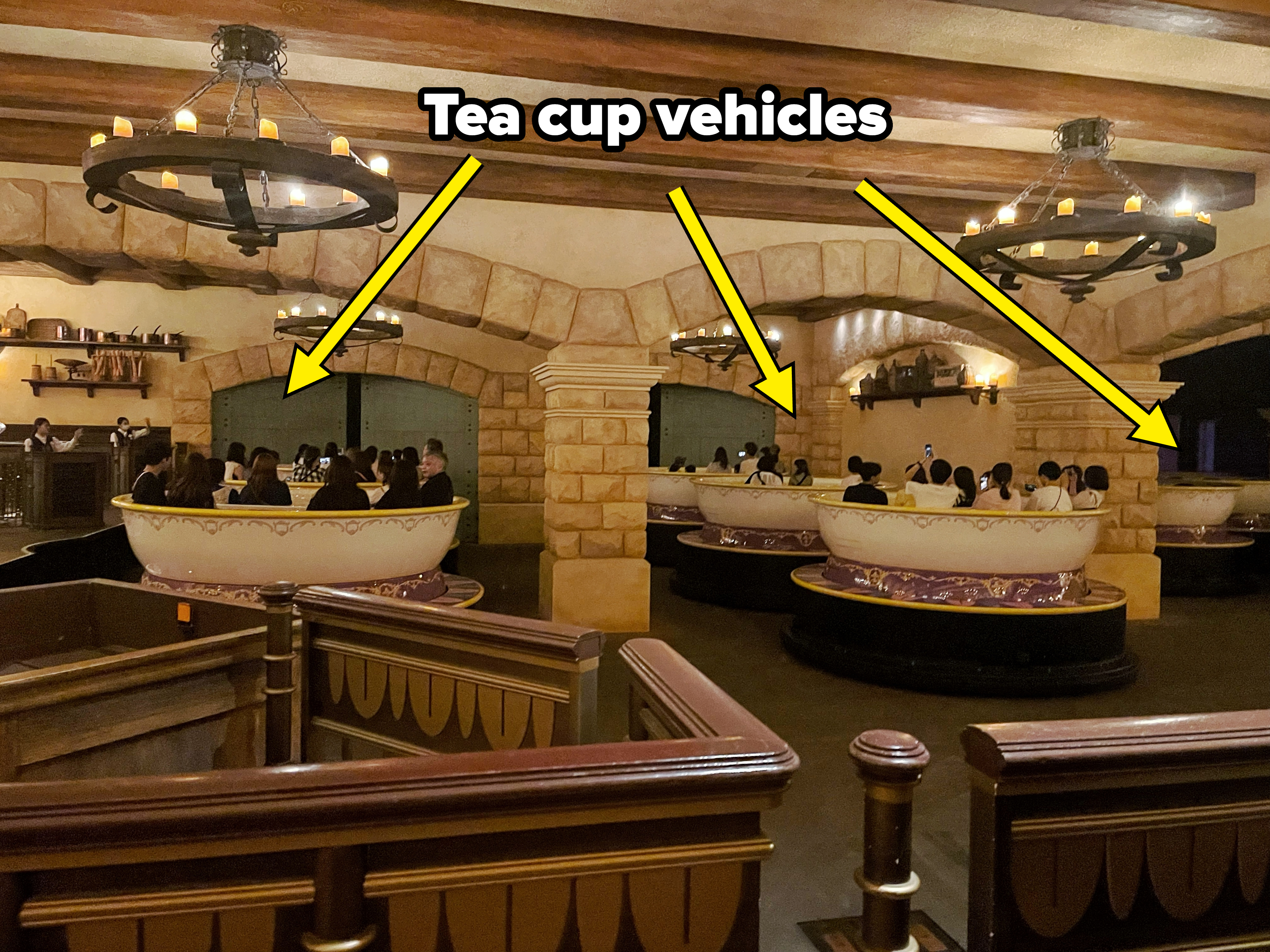 Ride with multiple large teacup-shaped cars on a rotating platform in an indoor setting, with people seated inside the teacups