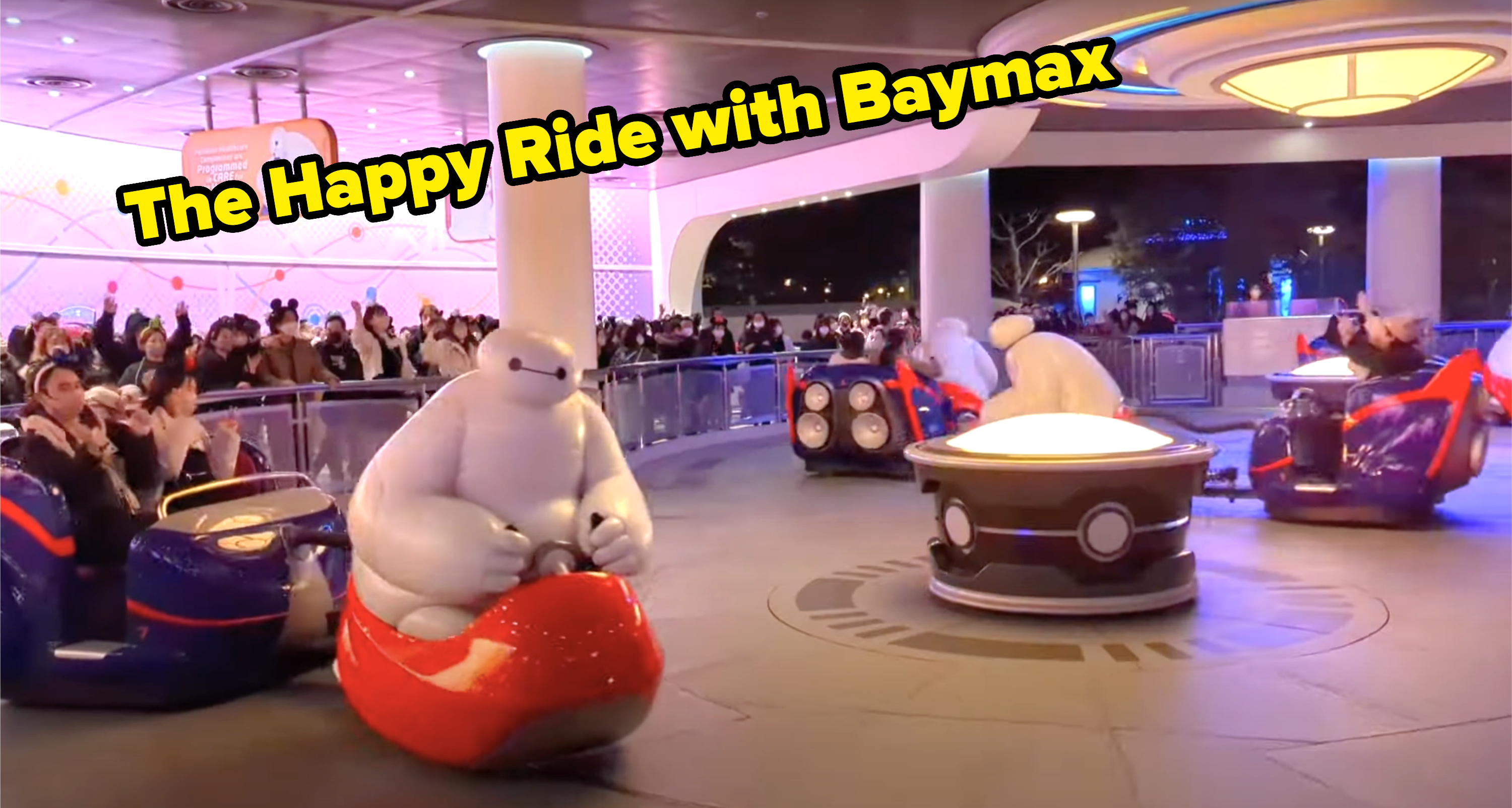 Guests enjoying the Baymax-themed ride at Disneyland, featuring Baymax-shaped cars spinning in a colorful, futuristic environment