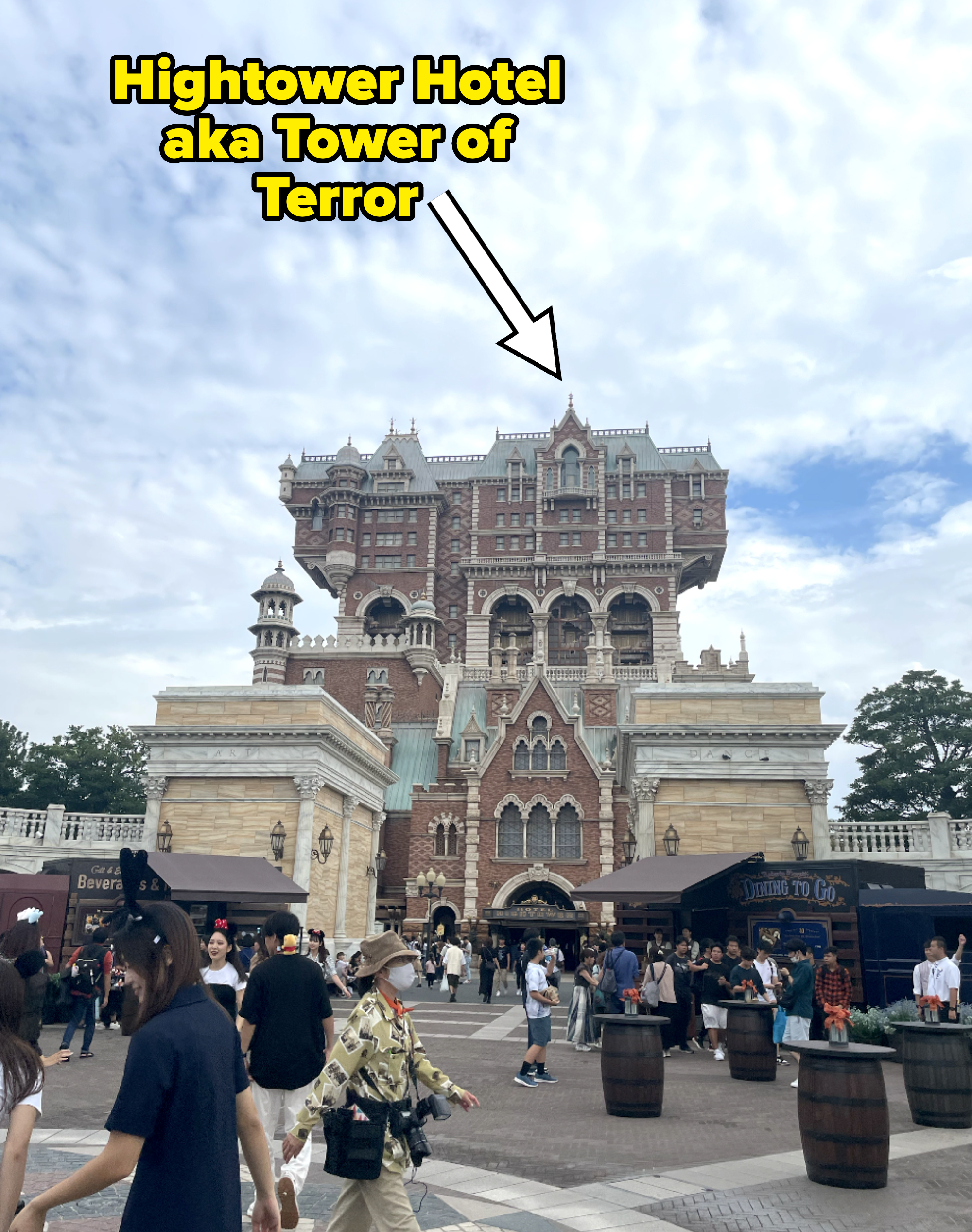 People walk in front of the Tower of Terror attraction at Tokyo DisneySea, surrounded by various booths and shops
