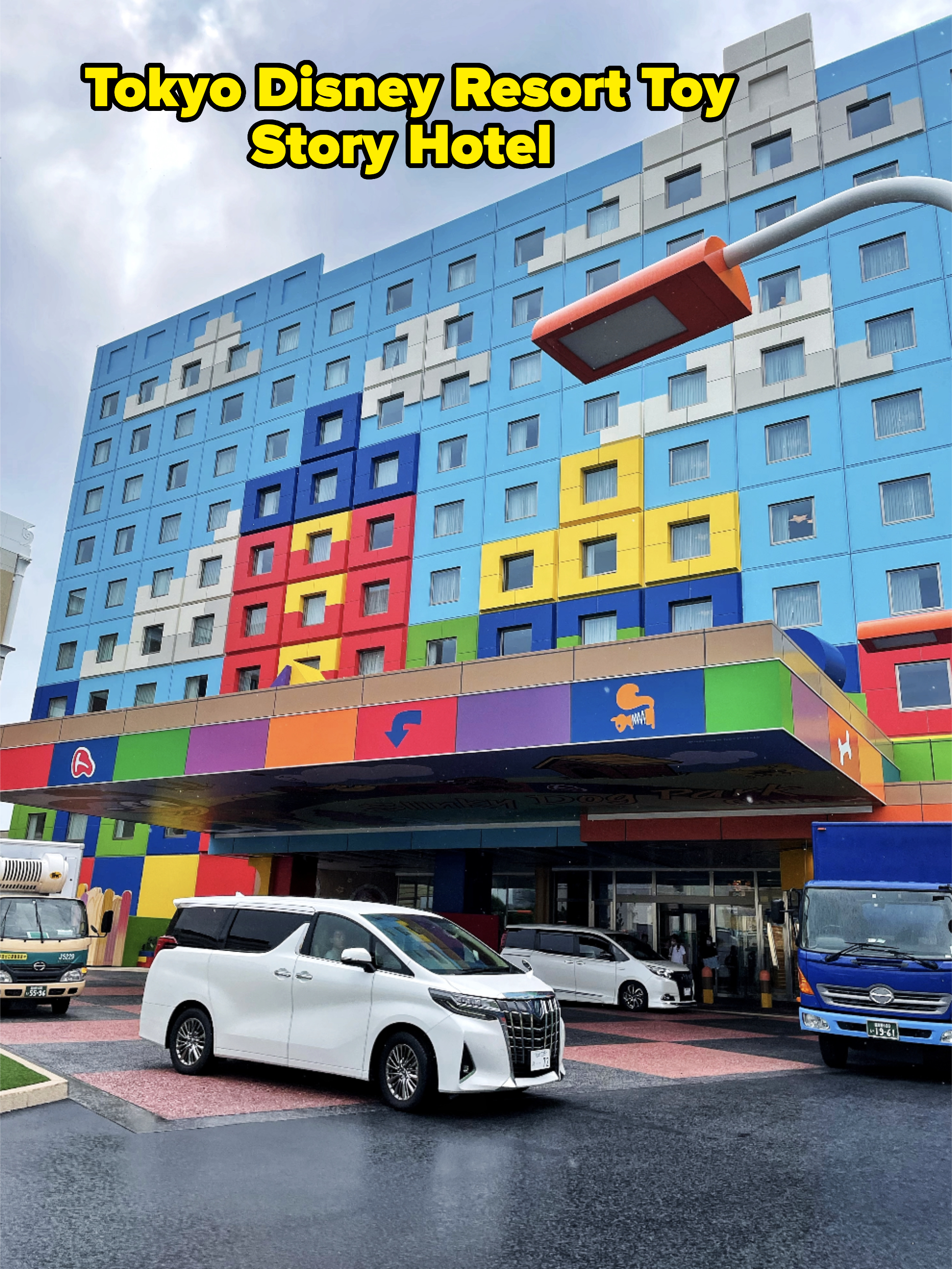 A colorful building with a playful facade and various vehicle logos. Two cars, one white and one blue, are in front of the building