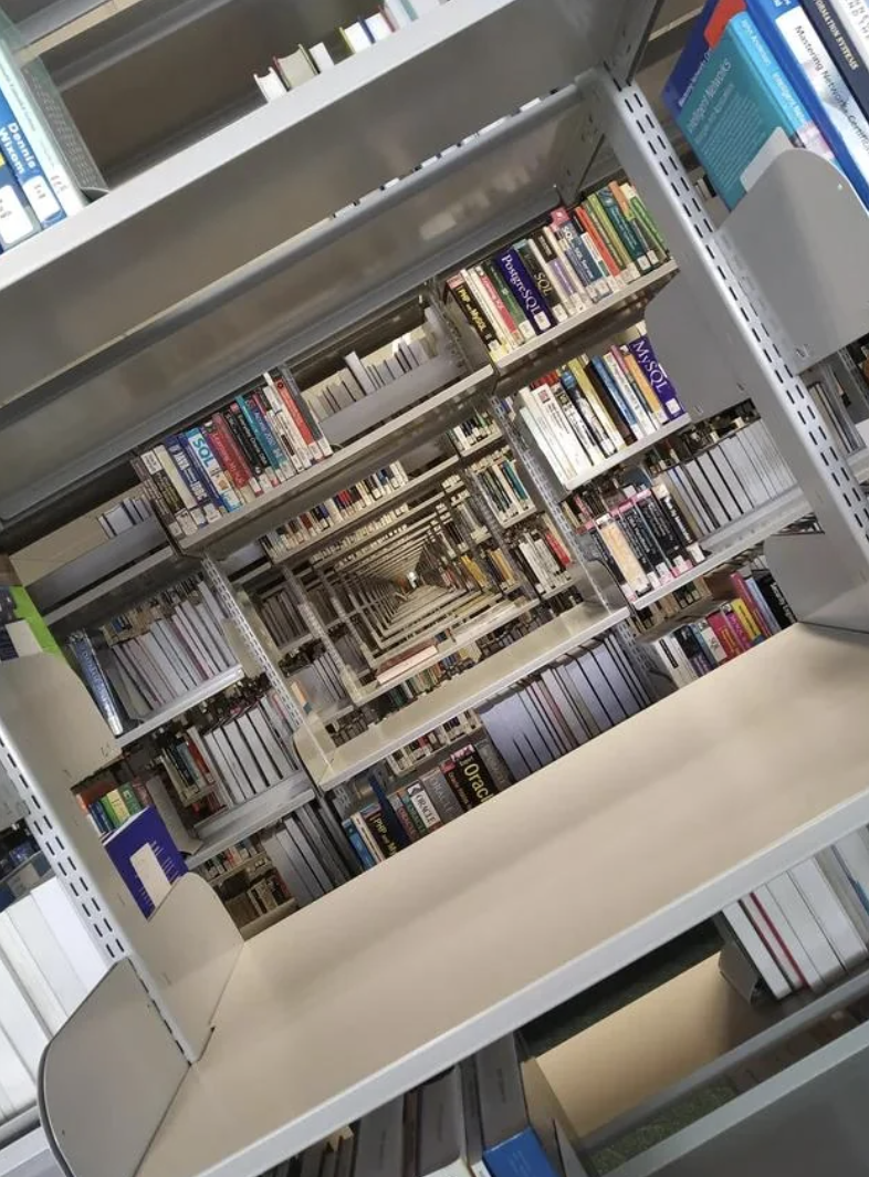 Library shelves filled with various books, creating an optical illusion of infinite depth due to the camera angle