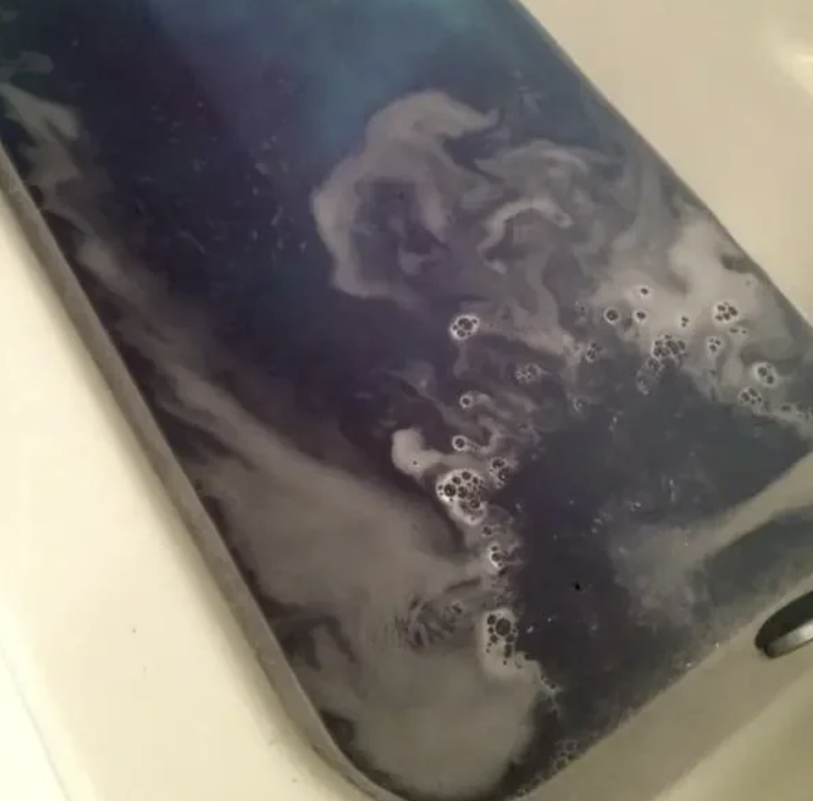 A close-up of a bathtub filled with dark water and bubbles, giving an impression of a bath bomb or special bath treatment. No people are in the image