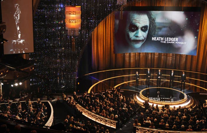 A large audience is gathered at an awards ceremony. On stage, a screen displays an image of Heath Ledger as the Joker from &quot;The Dark Knight&quot; and his name