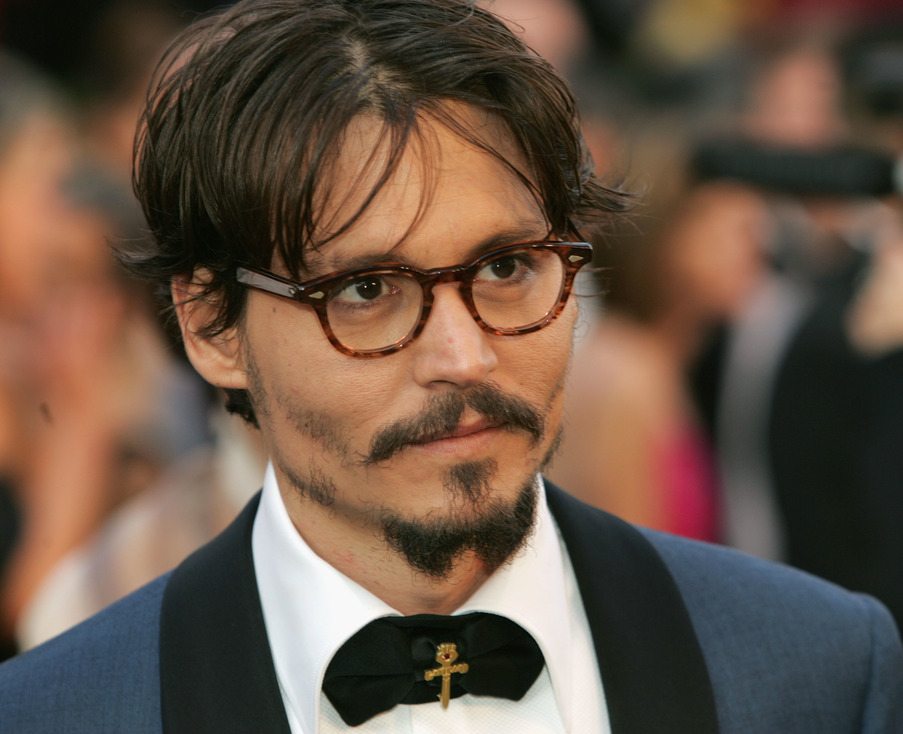 Johnny Depp, sporting glasses, a groomed mustache, and a goatee, wears a shirt with a bow tie and blazer at a formal event