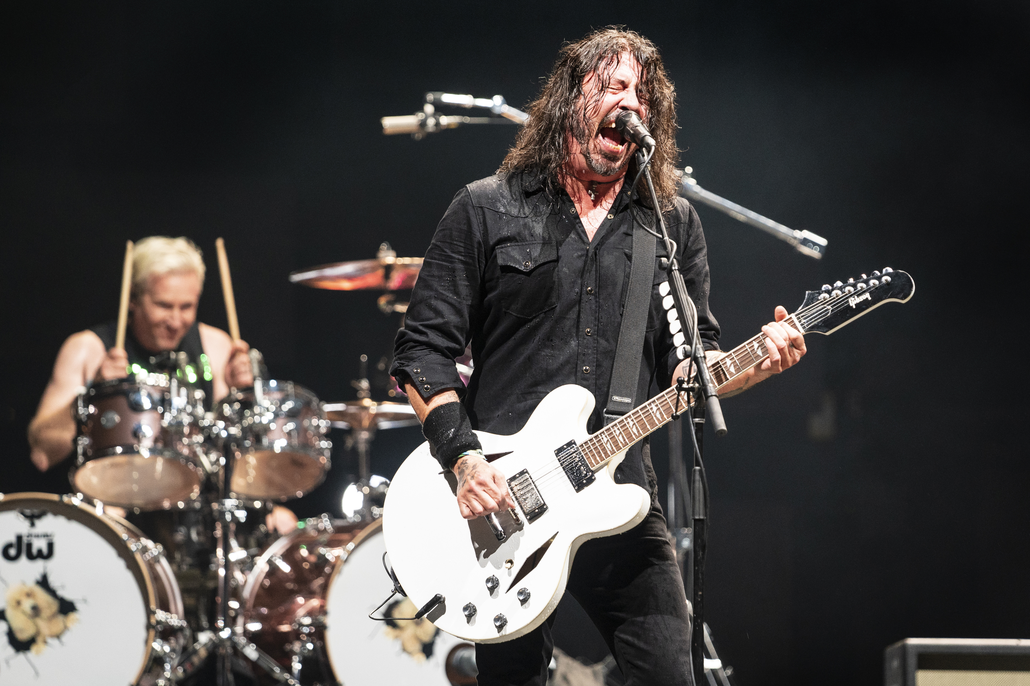 Dave Grohl passionately plays guitar and sings on stage while Taylor Hawkins energetically plays drums in the background