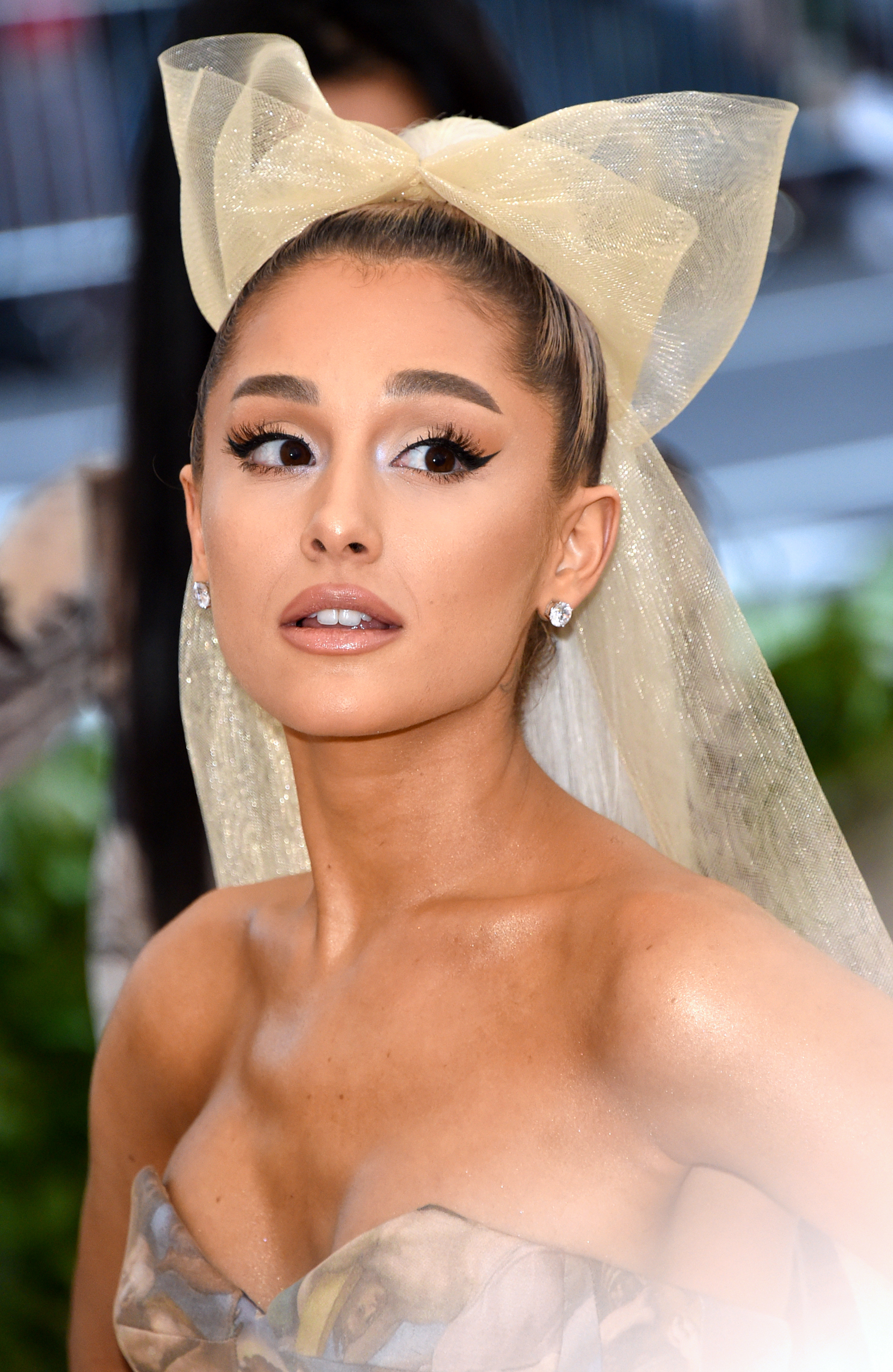 Ariana Grande is wearing a strapless gown and a large, sheer bow in her hair at a formal event