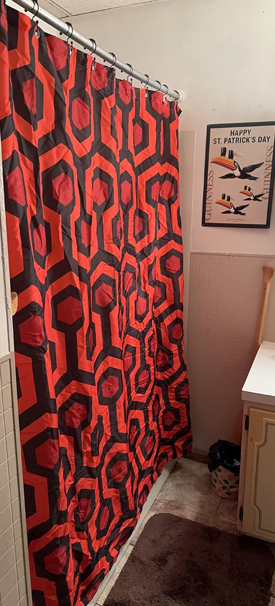 A bathroom with a red and black patterned shower curtain, a &quot;Happy St. Patrick&#x27;s Day&quot; poster on the wall, a counter, and floor mats