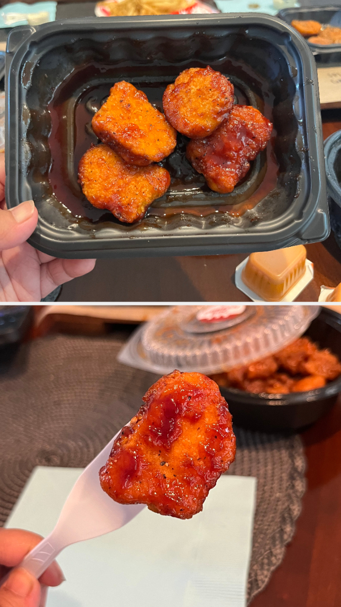 Person holding a black container with four pieces of sauced chicken nuggets; another close-up of a single nugget on a plastic fork. Several food items in the background