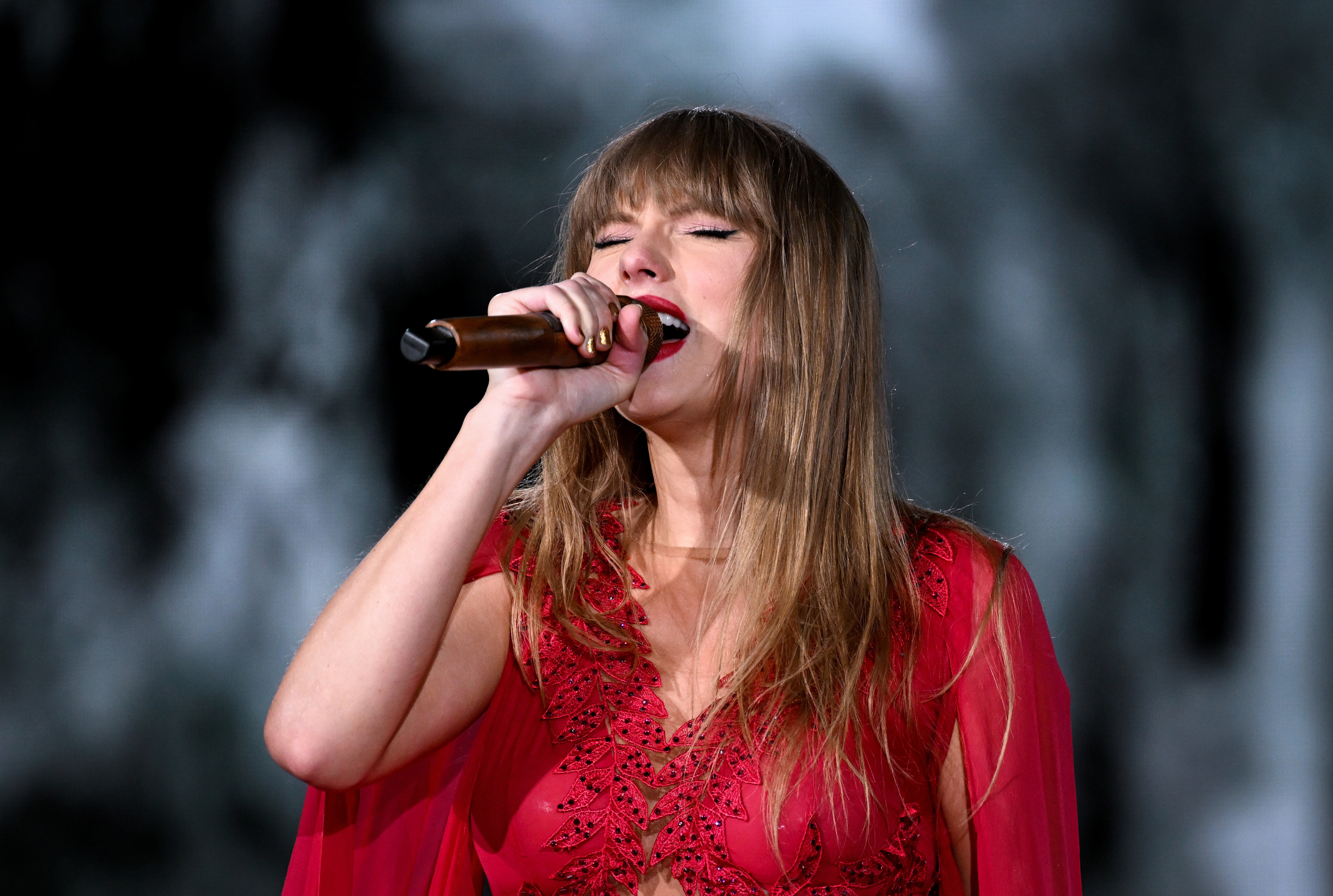 Taylor Swift passionately singing into a microphone while wearing a detailed, flowing gown