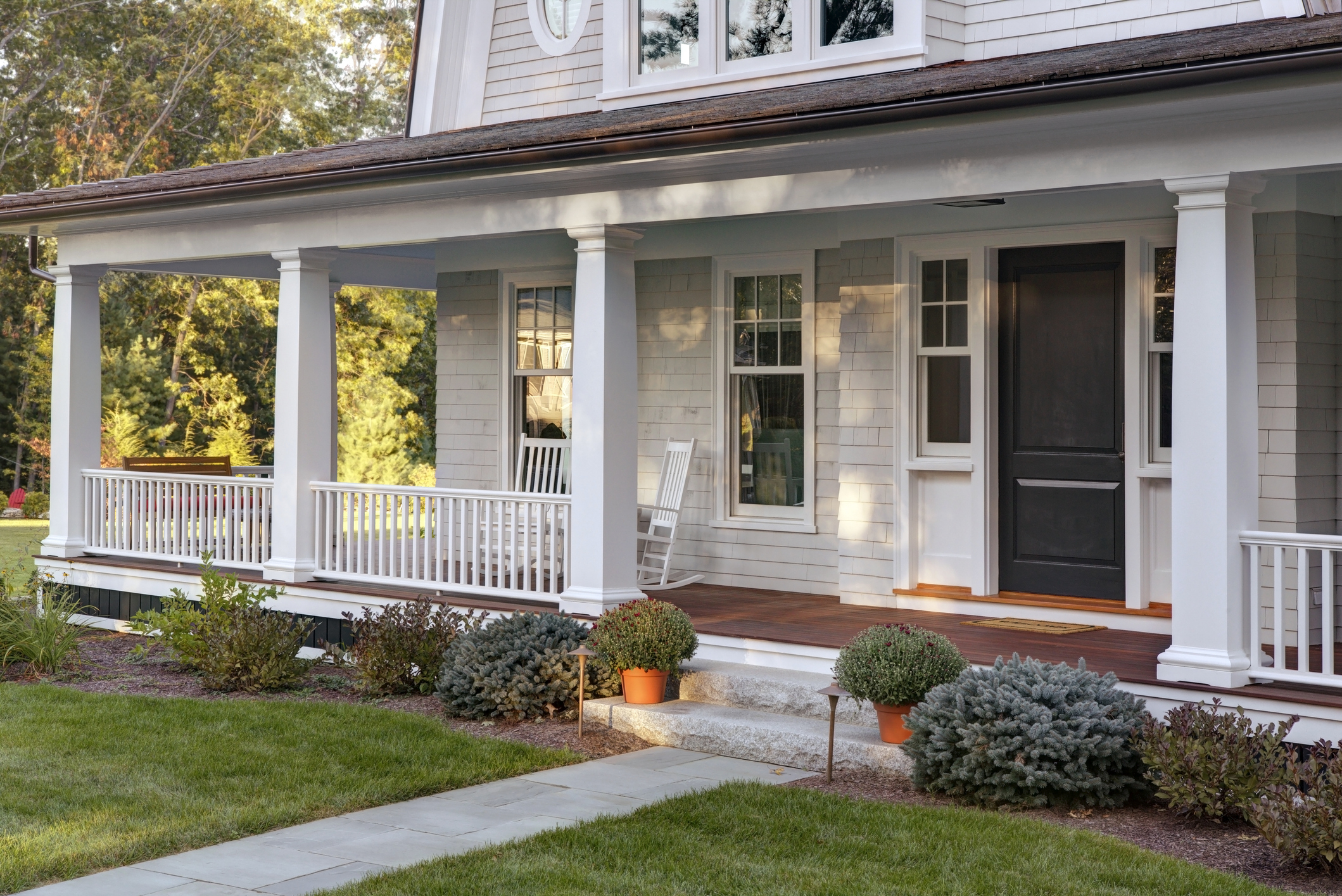 A cozy house with a front porch featuring columns, a rocking chair, potted plants, and a neatly manicured lawn