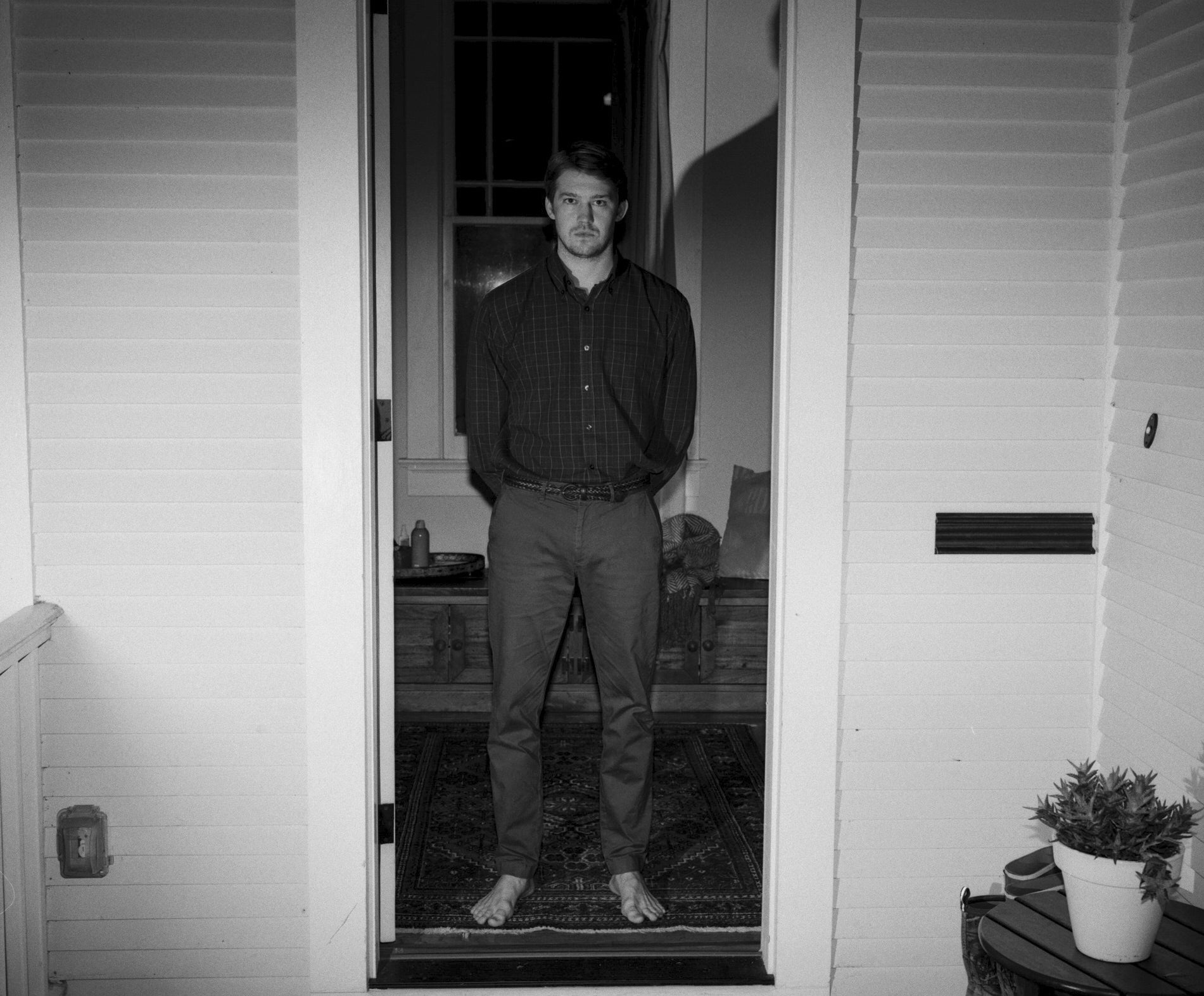 Joe Alwyn standing barefoot in a doorway in Kinds of Kindness