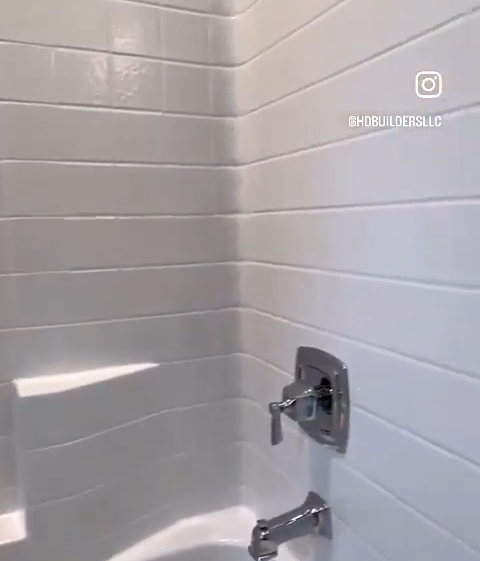 White-tiled bathroom corner with chrome faucet and showerhead, featuring @HDbuildersLLC watermark on the wall