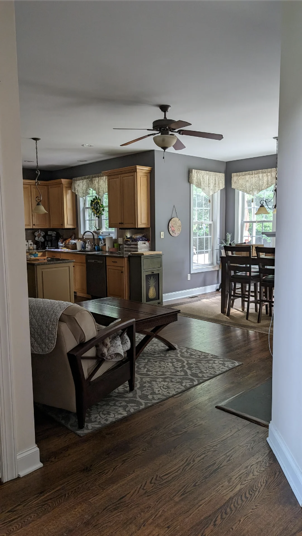 Modern living room with an armchair, coffee table, and a kitchen in the background, complete with wooden cabinets and a dining table by the windows