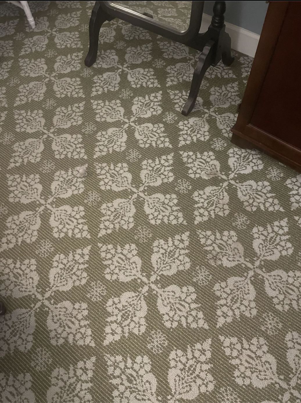Patterned carpet with a floral design, part of a mirror leg, and a piece of furniture visible at the edge