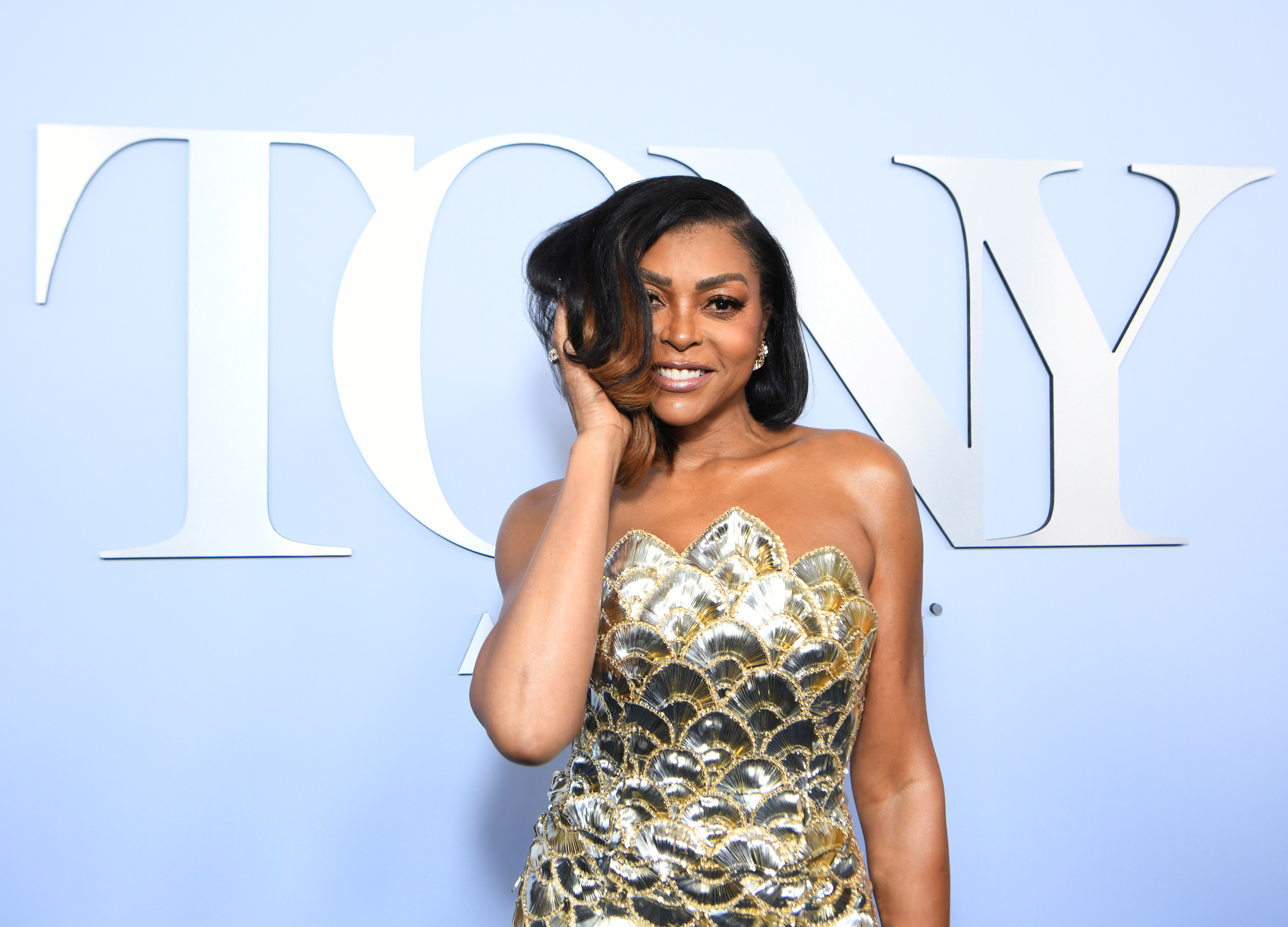 Taraji P. Henson poses in front of &quot;TONY&quot; sign in a strapless, sequined gown with a scallop pattern. She smiles with one hand touching her hair