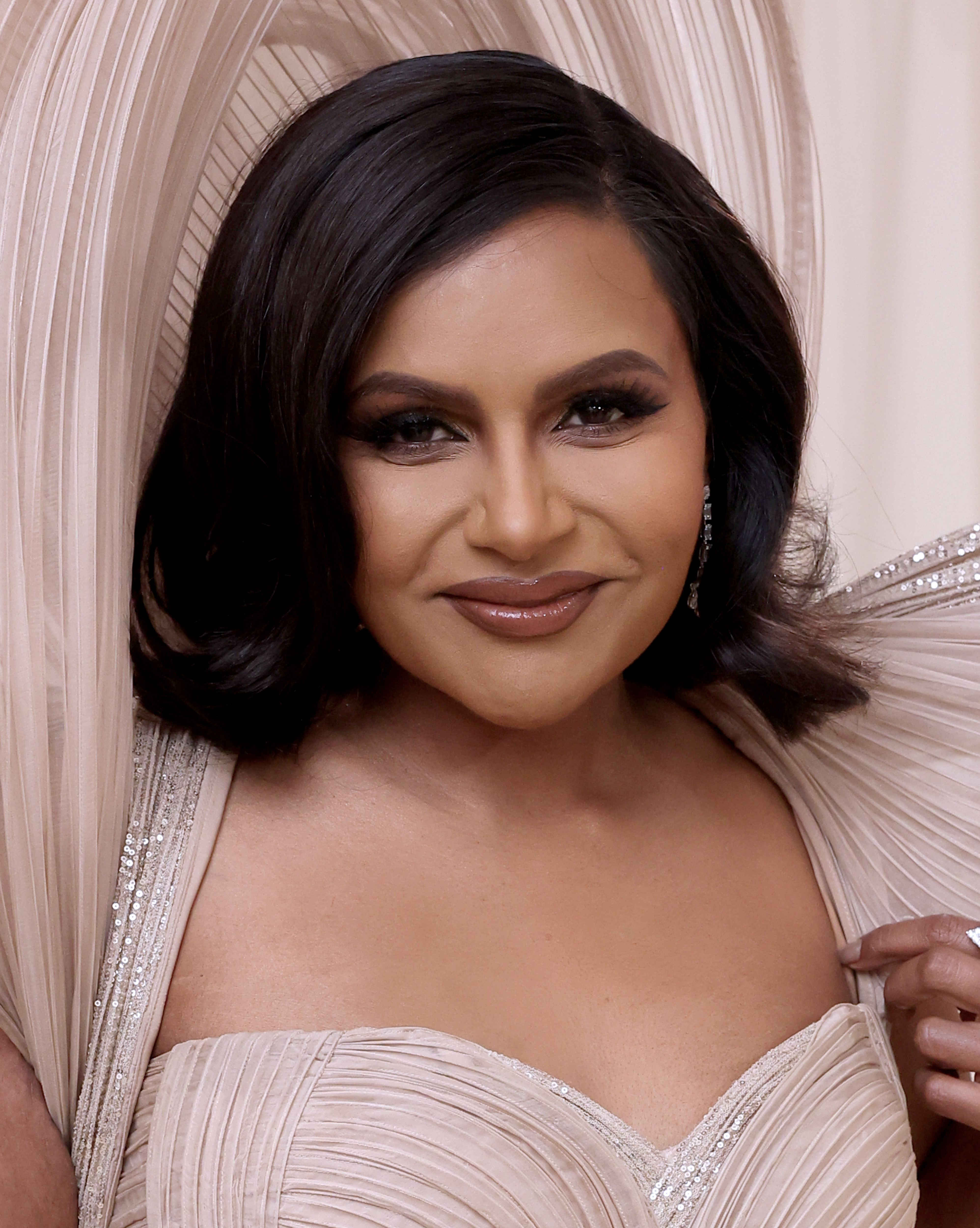 Mindy Kaling in a pleated gown with large structured shoulders, smiling at the camera
