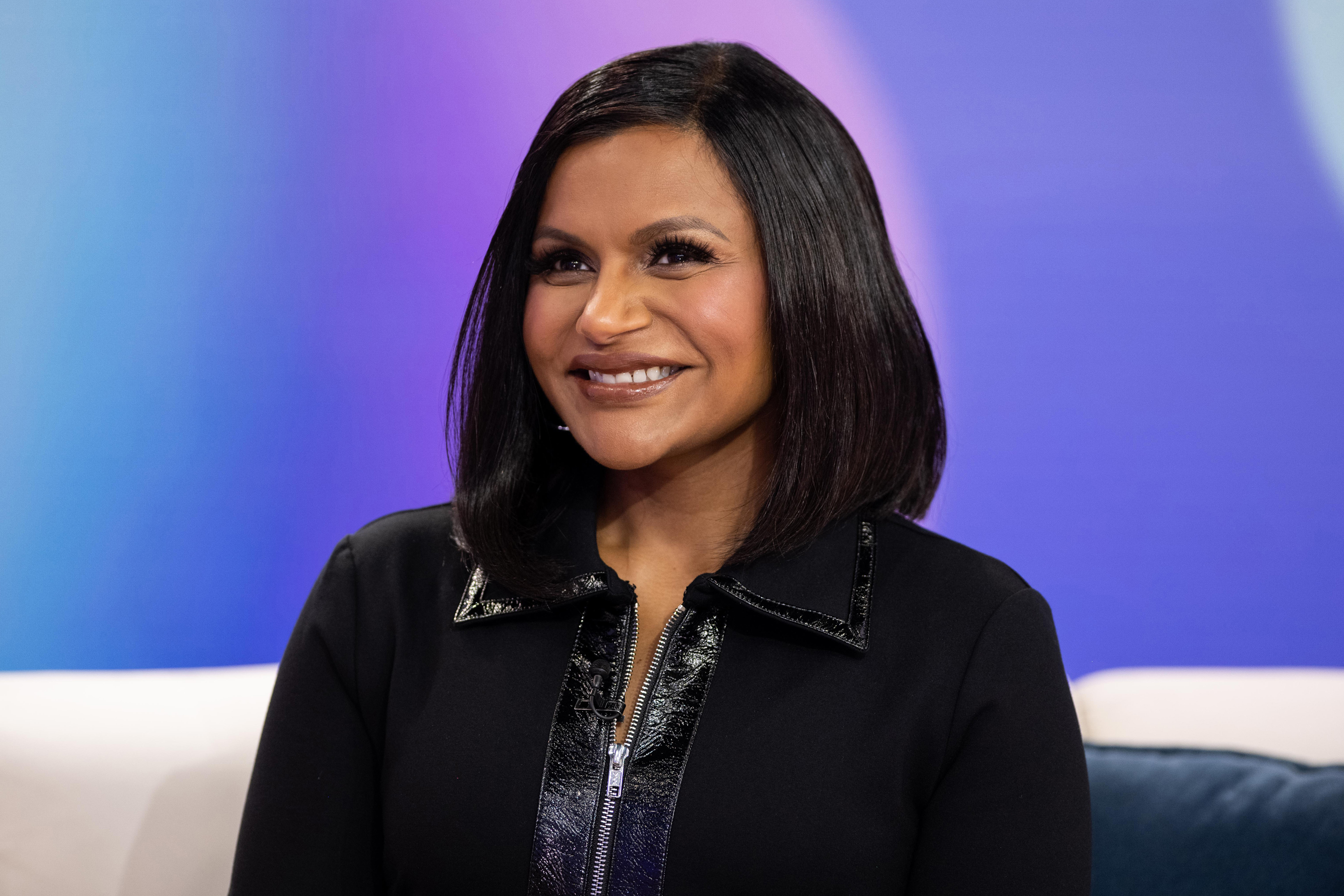 Mindy Kaling smiles while seated for a studio interview