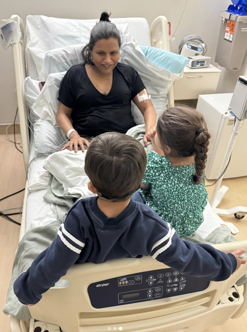 Mindy Kaling in the hospital with her two children sitting on the bed with her