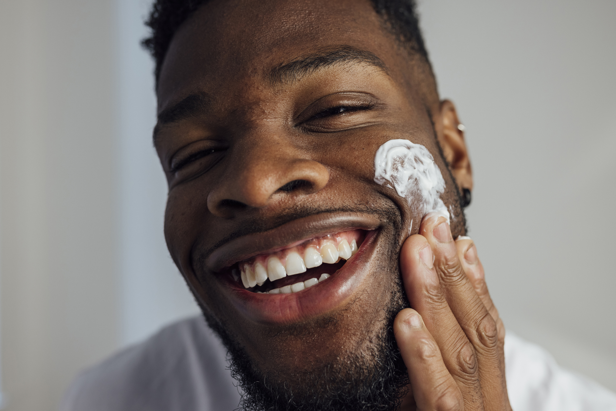 A person smiling and applying moisturizer to their face, highlighting a skincare routine