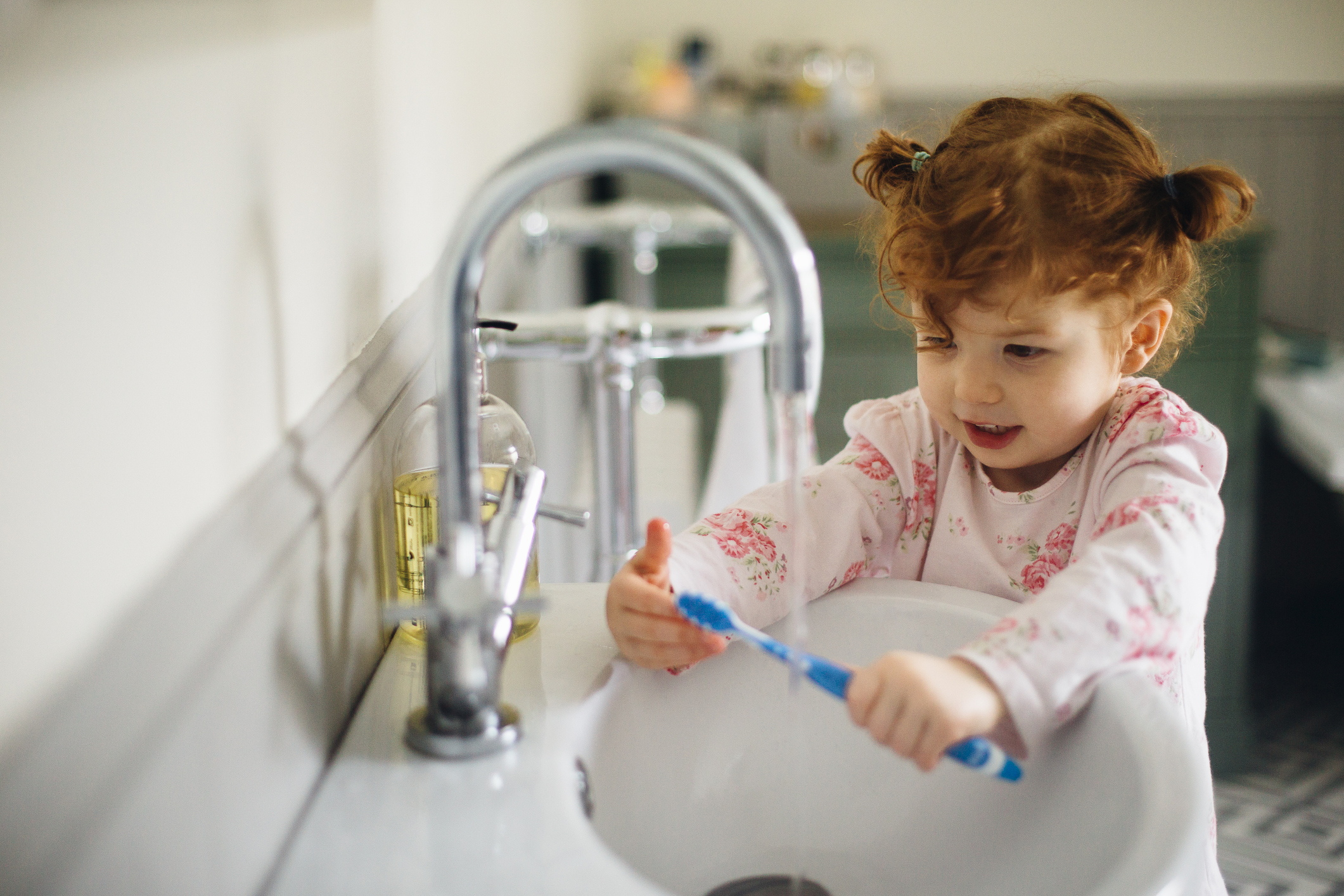 Young child with curly hair brushing teeth at a bathroom sink