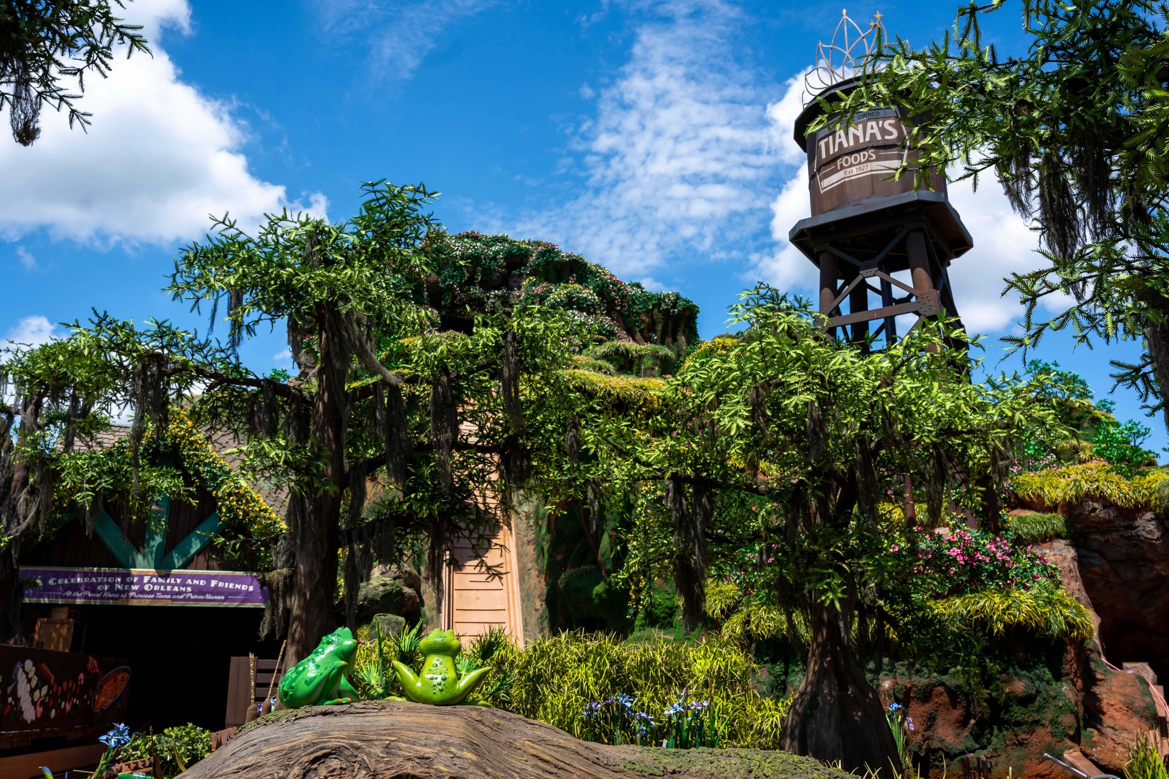 Walt Disney World&#x27;s Splash Mountain re-themed as Tiana&#x27;s Bayou Adventure. The ride&#x27;s exterior features lush greenery and a water tower labeled &quot;Tiana’s Foods.&quot;