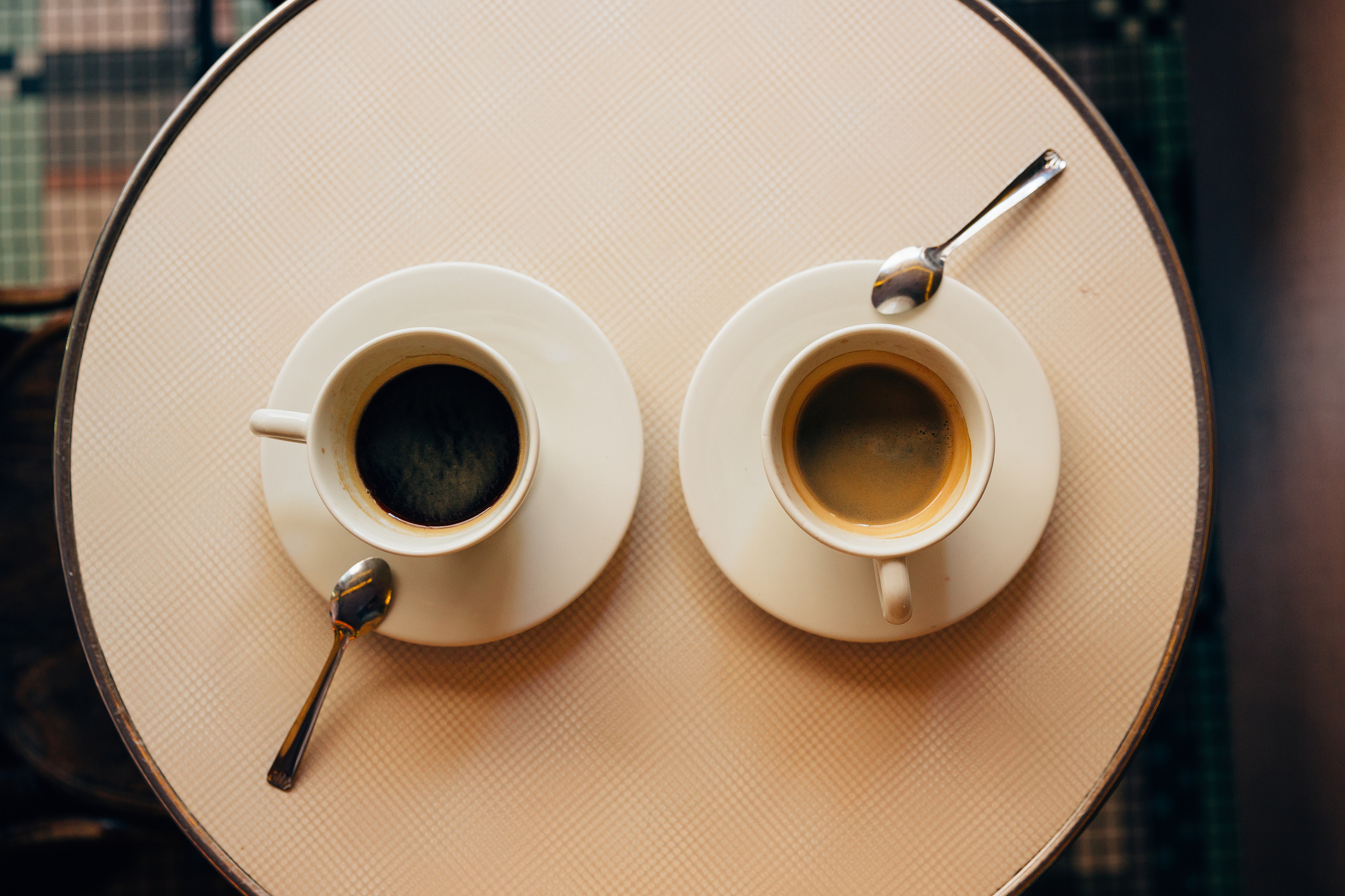 Two cups of coffee with spoons on the saucers are placed on a round table, viewed from above