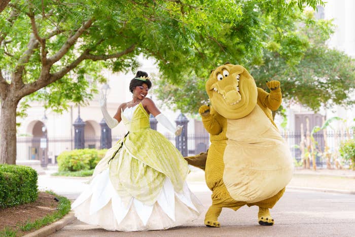 Tiana and Louis from &quot;The Princess and the Frog&quot; happily pose together outdoors, with Louis playfully outstretching his arms
