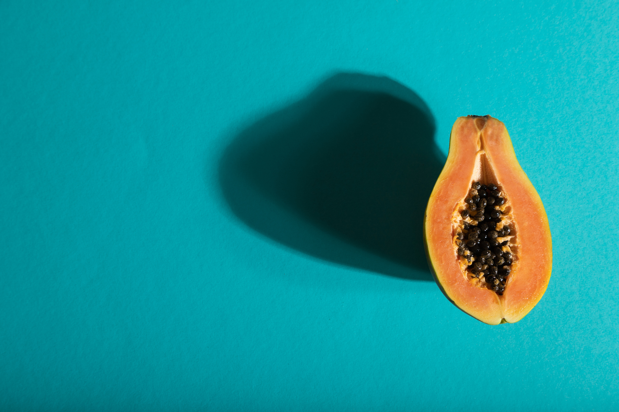 Half of a papaya with black seeds, casting a shadow, placed on a blue background